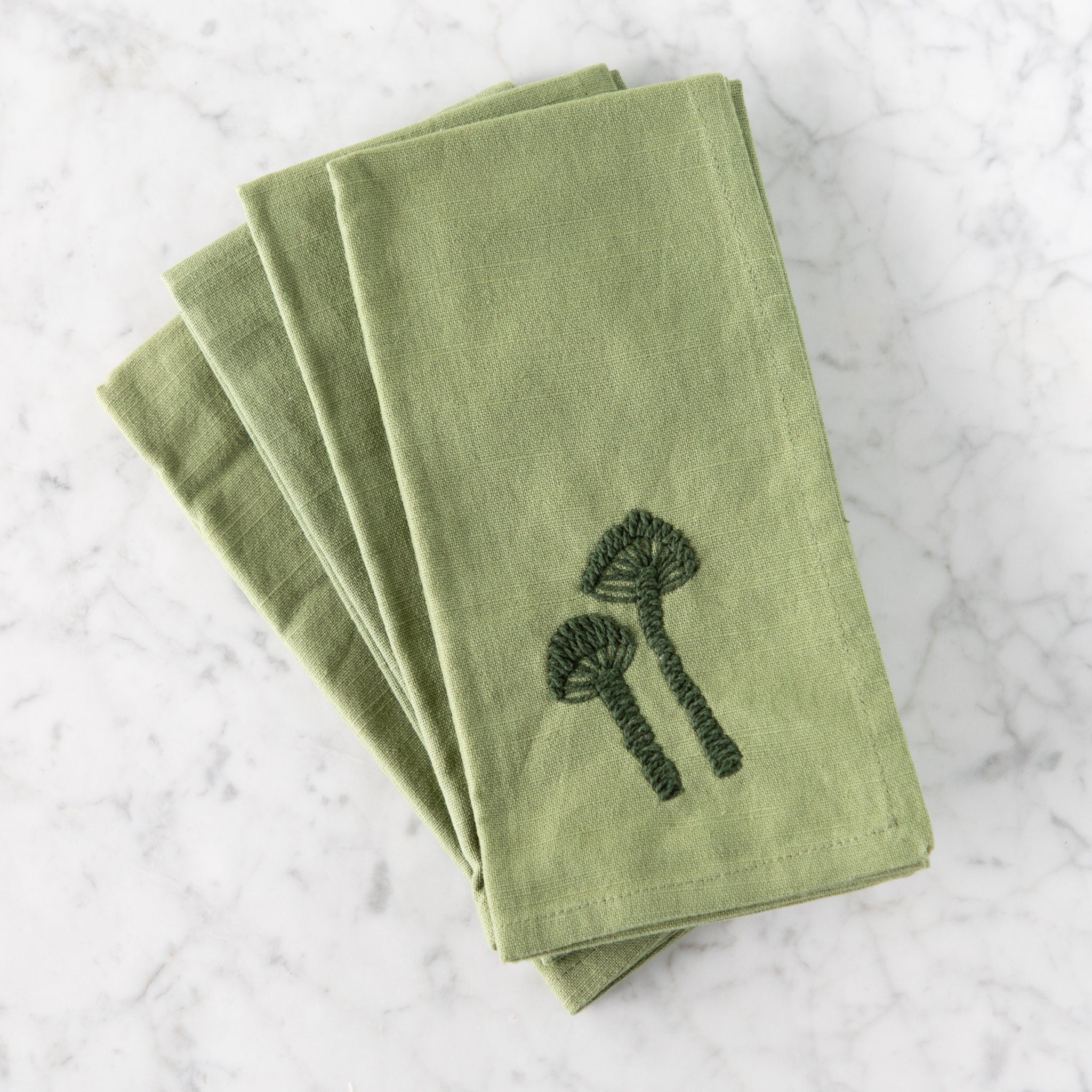 Set of green napkins with embroidered mushrooms on a marble surface.