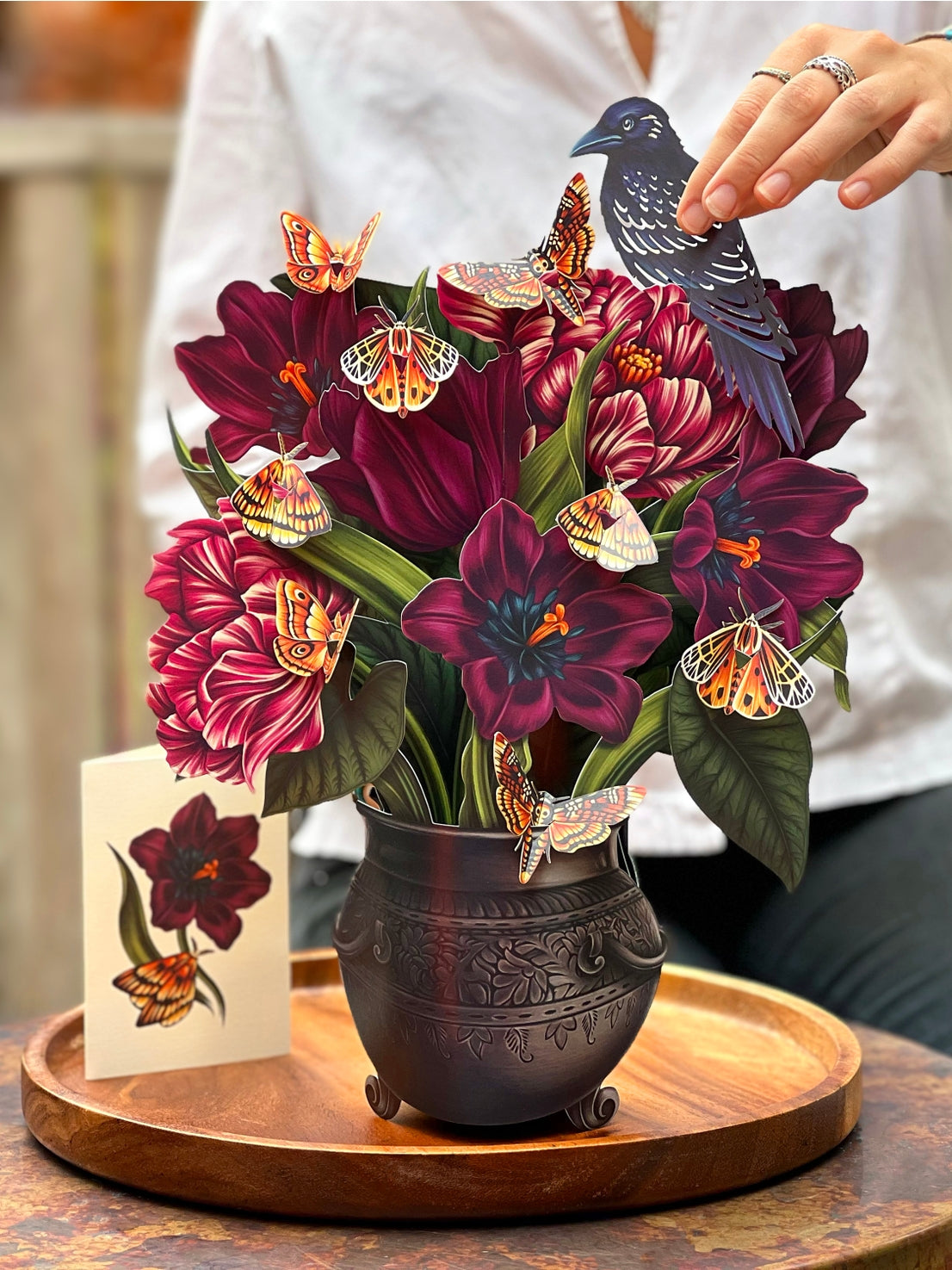 Decorative paper flower arrangement with butterflies and a bird on a wooden tray.