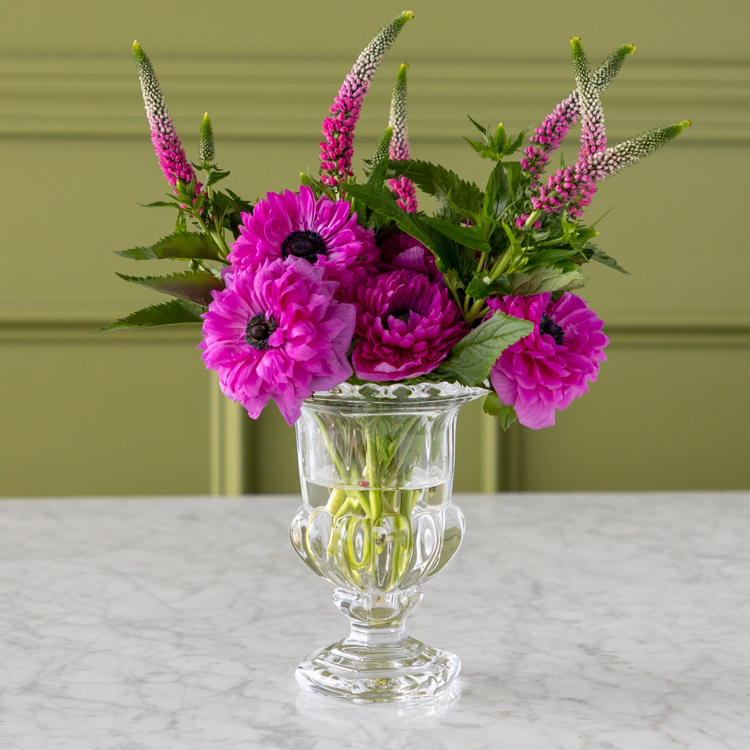 Clear glass vase with pink flowers on a marble surface and green background