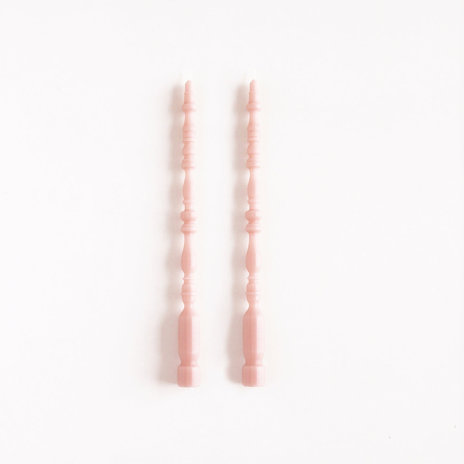 2 taper candles shaped like table spindle legs in rosewater. 