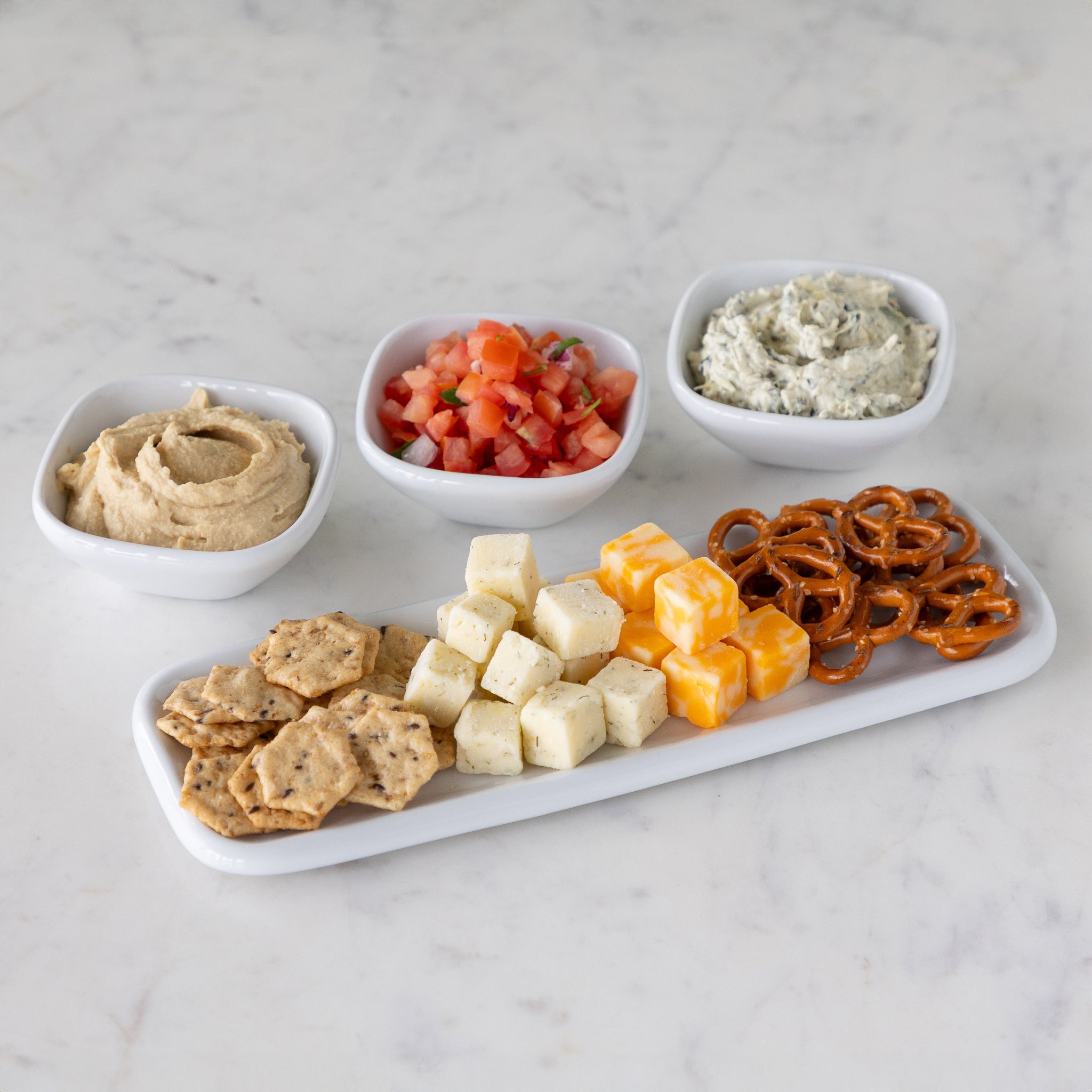 Platter with various snacks and three white bowls behind it filled with dips.