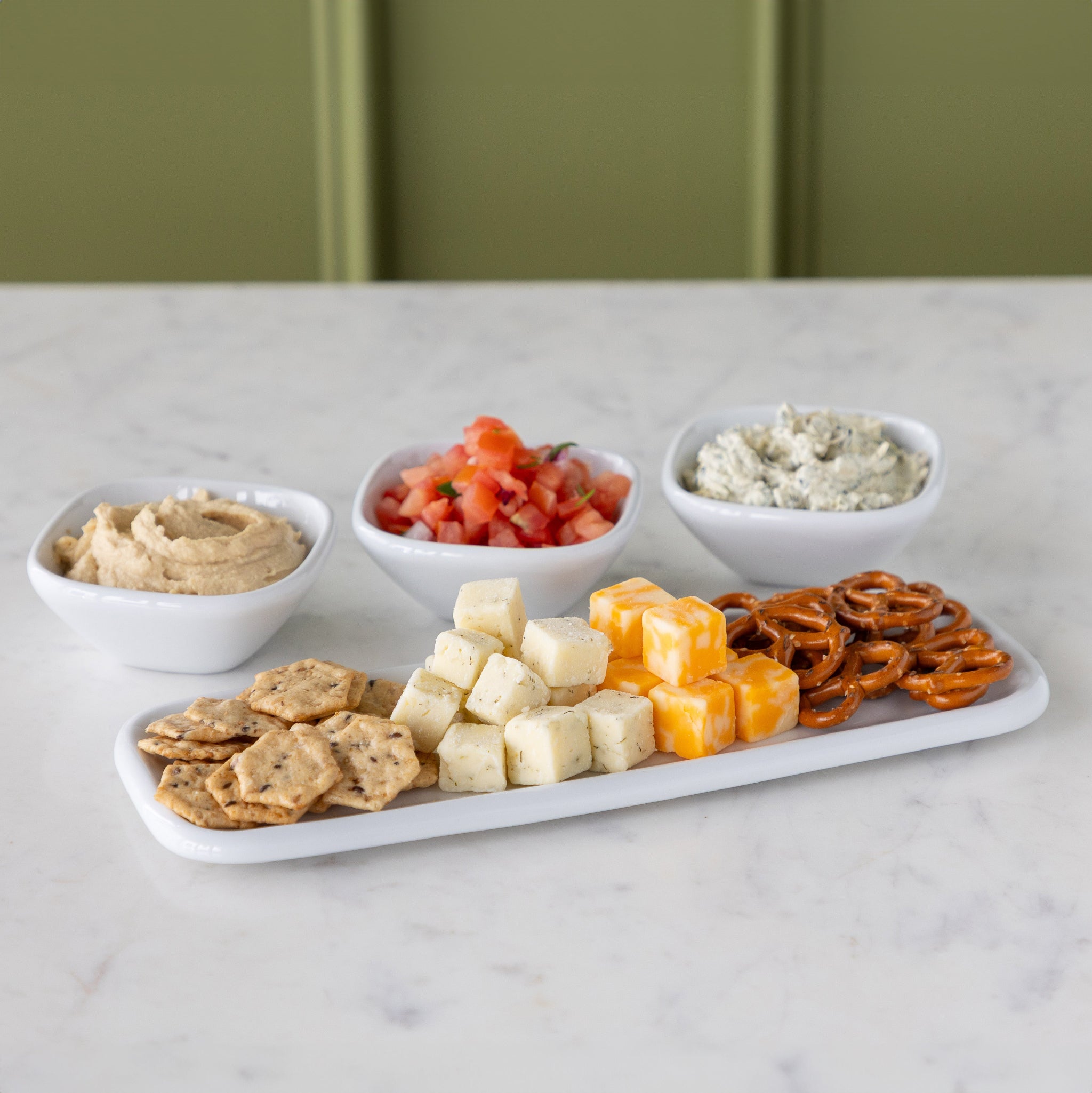 Platter with various snacks and three white bowls behind it filled with dips.