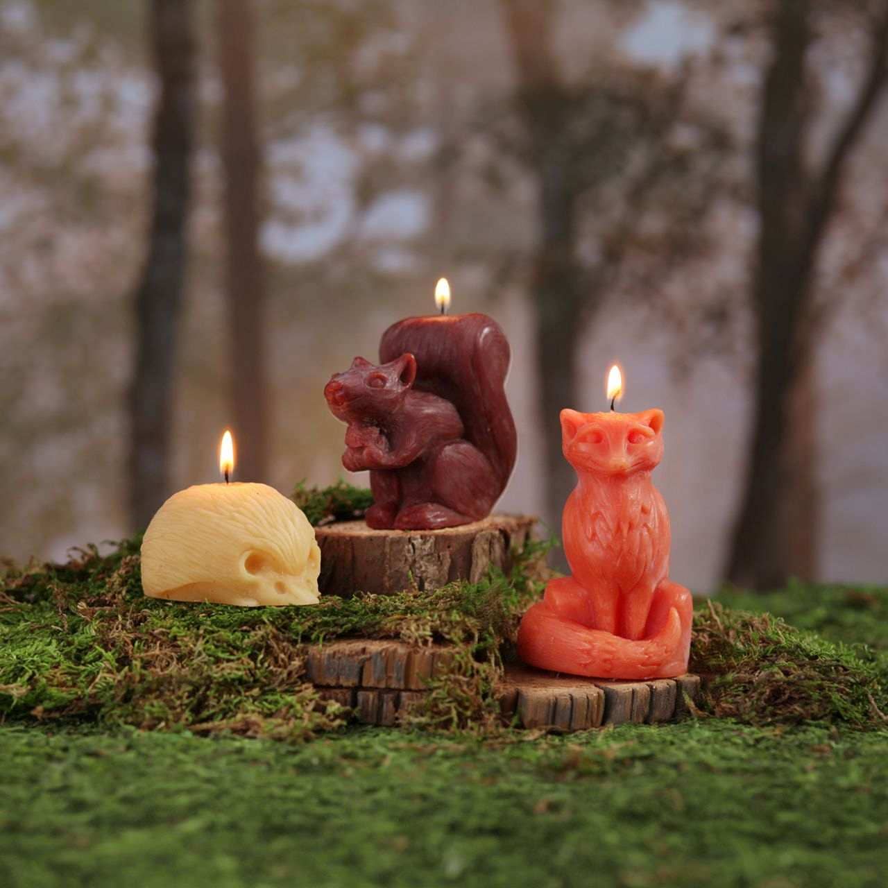 Three animal-shaped candles on a forest floor with blurred trees in the background