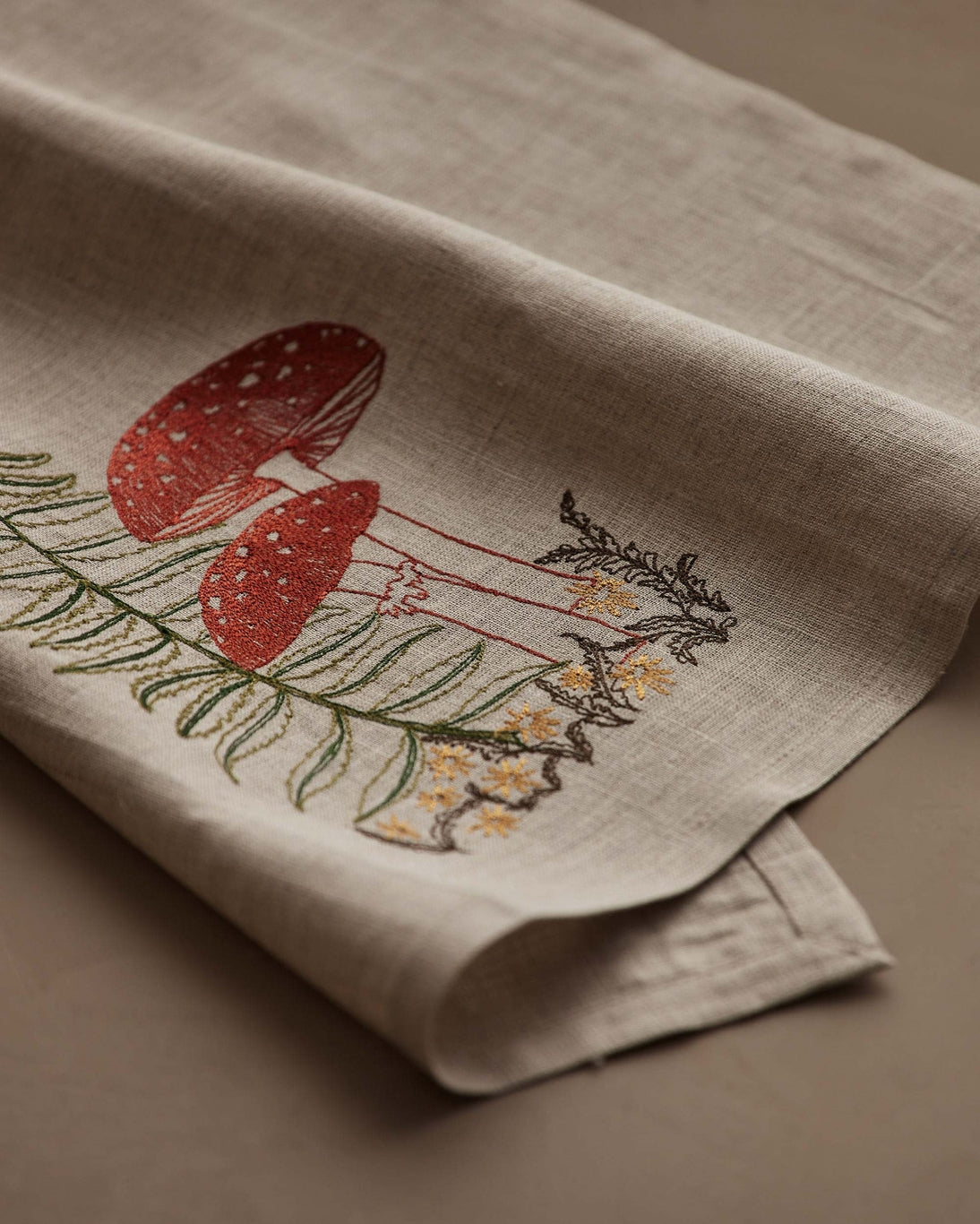 Embroidered towel with red mushrooms and green leaves on a beige background