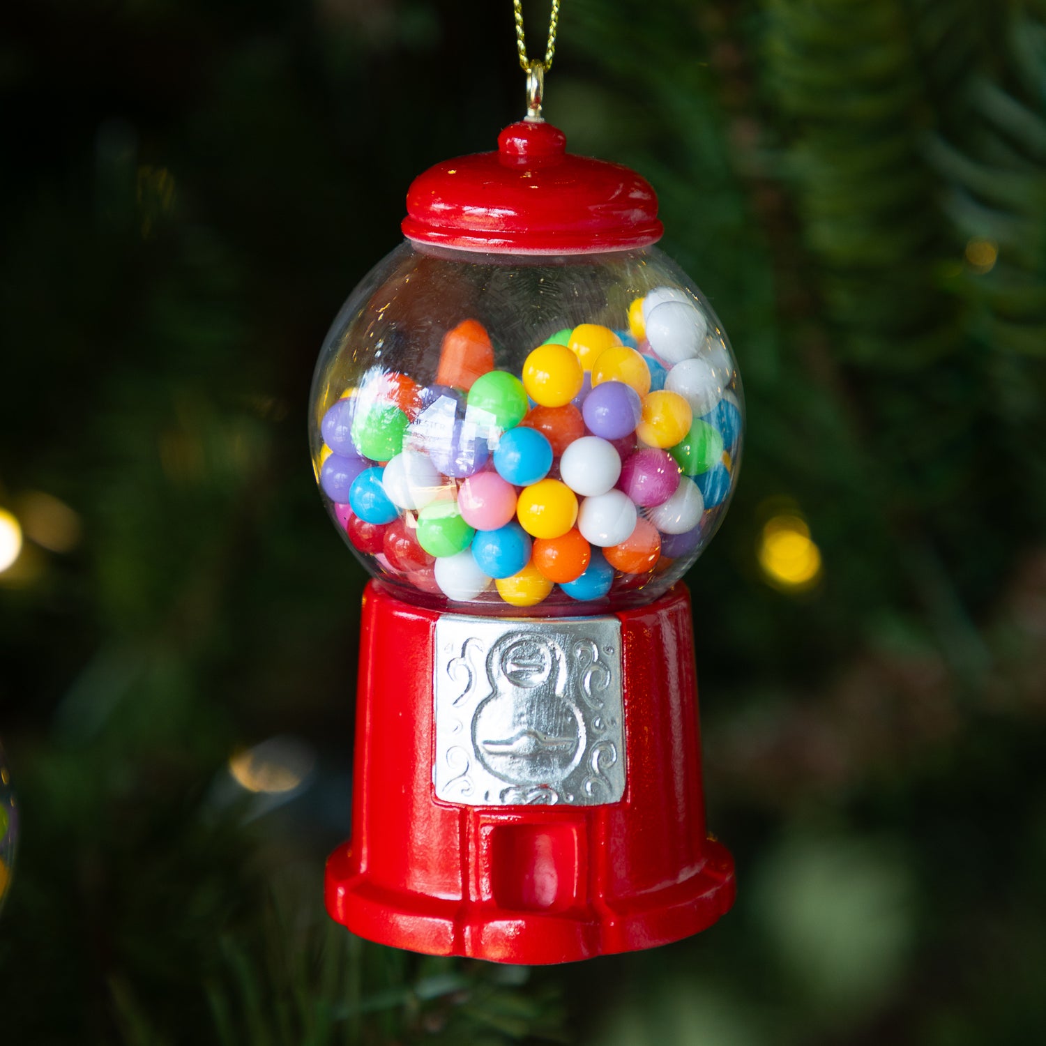 Red gumball machine ornament with colorful gumballs on lit Christmas tree.