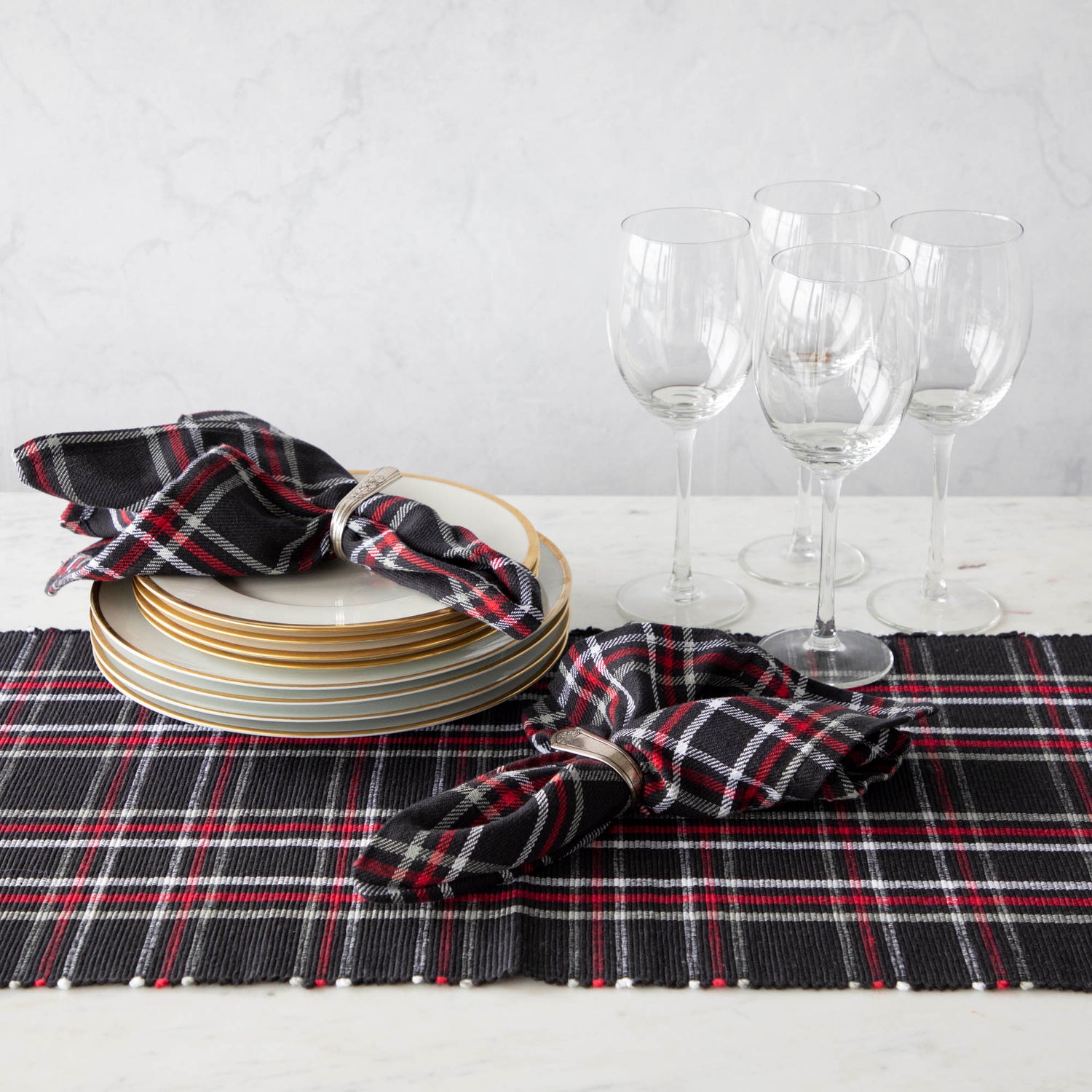 Two red plaid cotton napkins in napkin rings, displayed on a table with a matching plaid runner. 