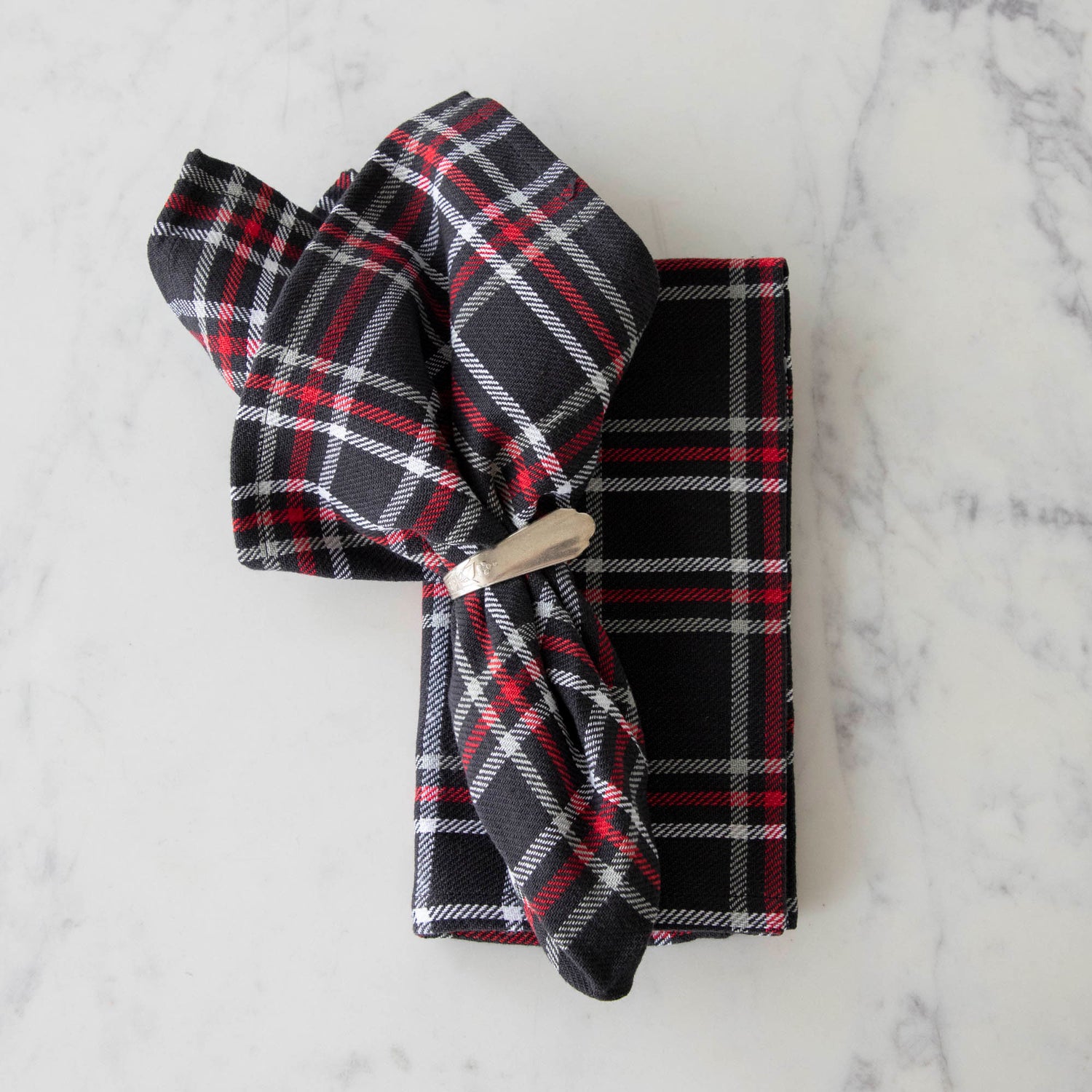 Two black plaid cotton napkins, one folded and one in a napkin ring, displayed on a white surface.