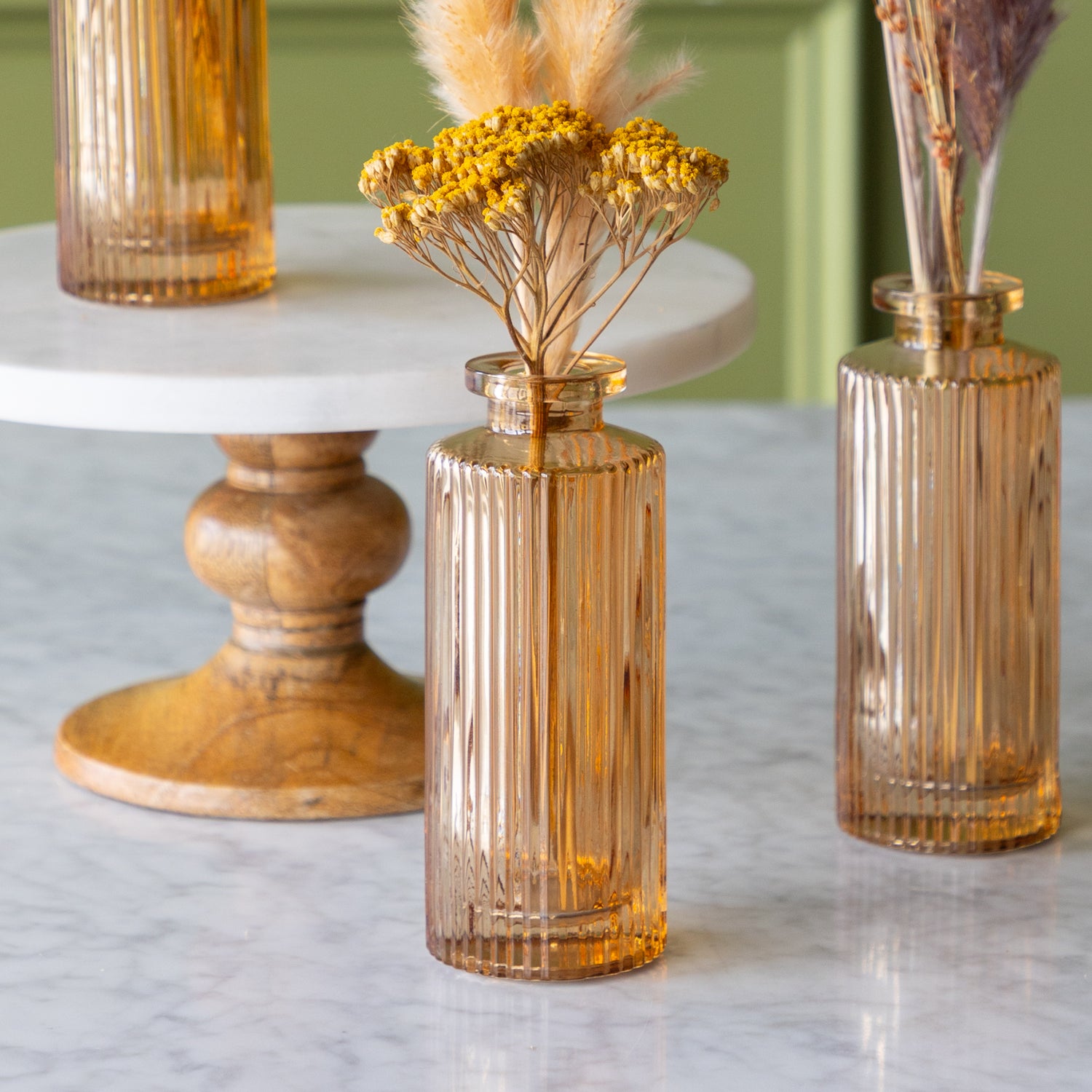 Amber glass vases with dried flowers on a marble surface.