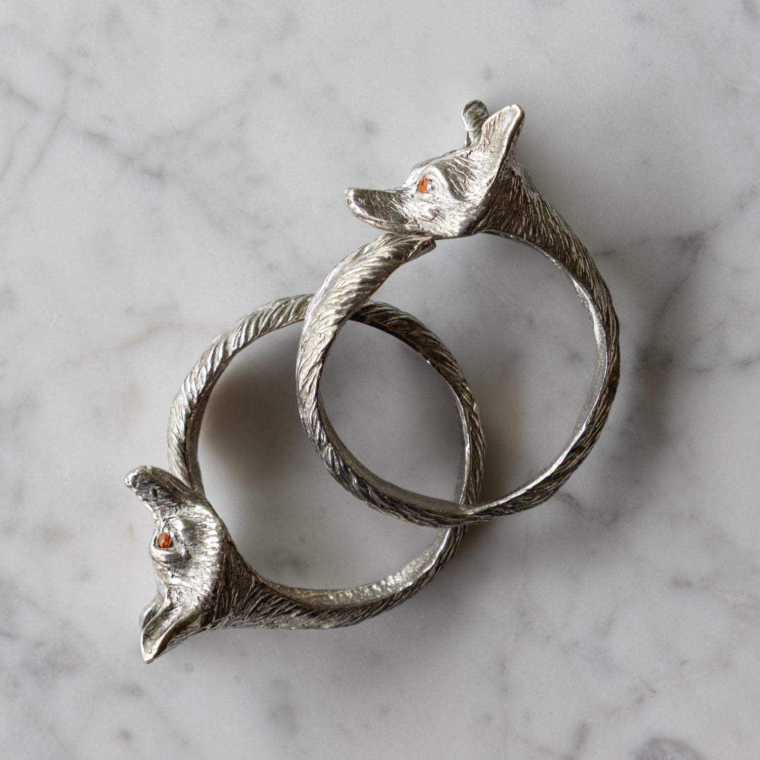 Two silver fox-shaped napkin rings on a marble surface.