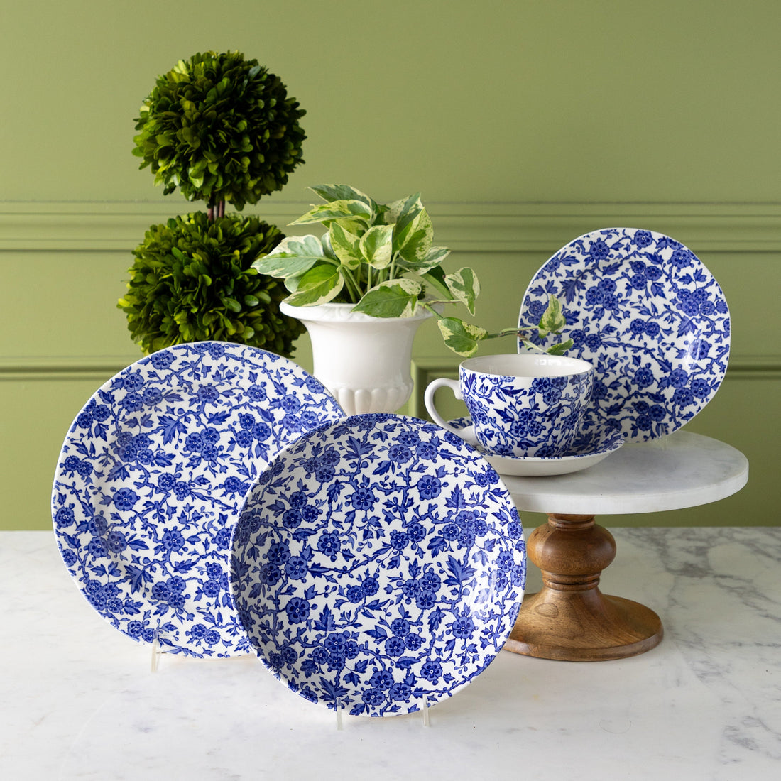 Burleigh Blue Arden Dinnerware displayed on a marble table with plants behind them.