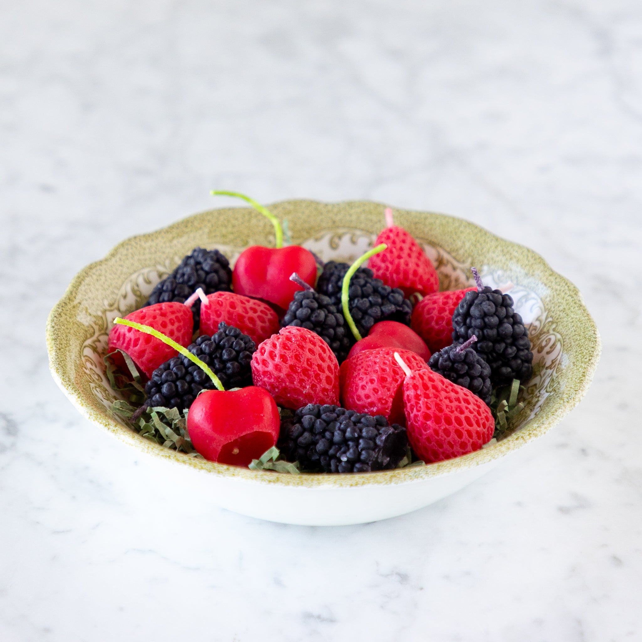 A decorative bowl filled with strawberry, blackberry and cherry shaped candles.