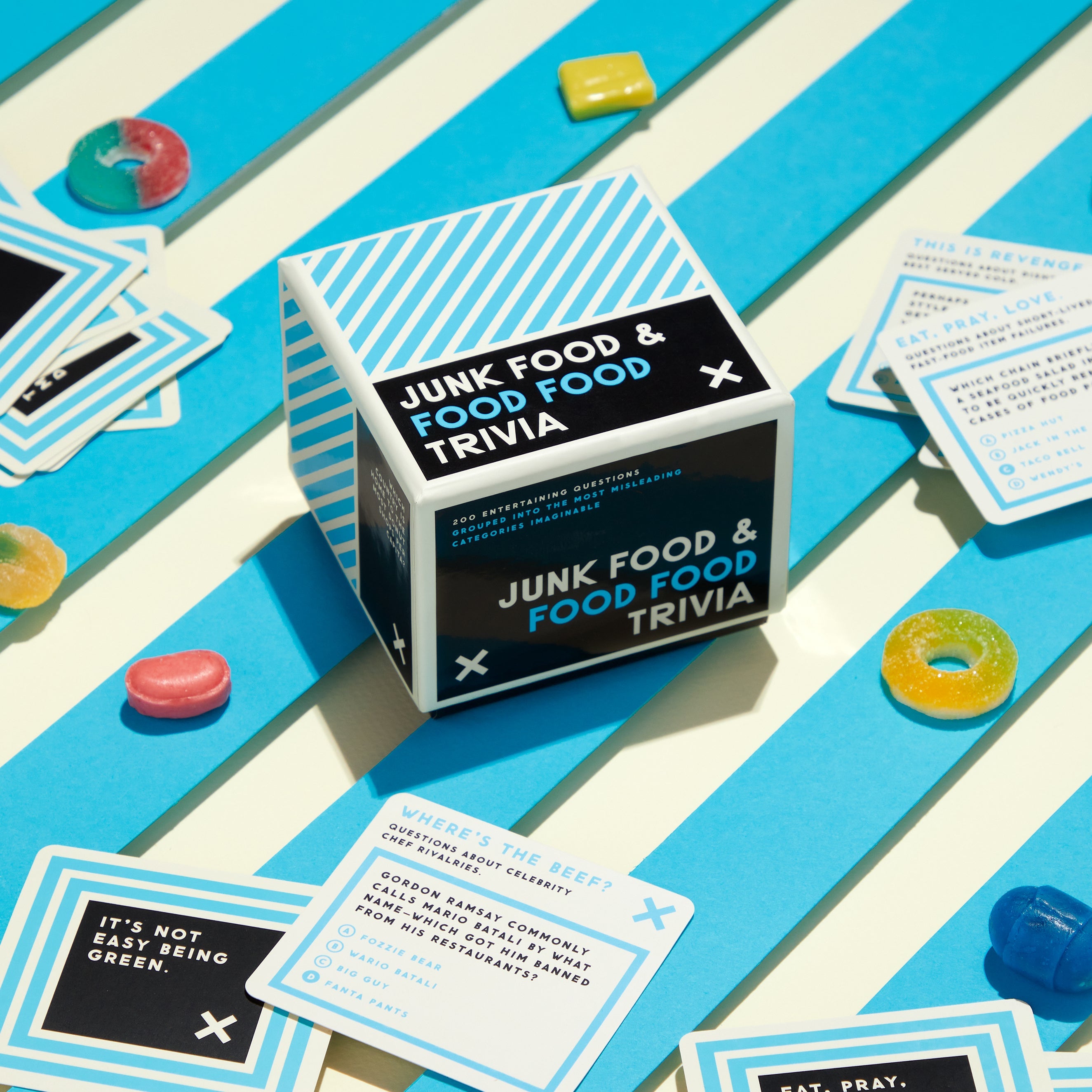 Game box on blue striped background with candy and game cards scattered