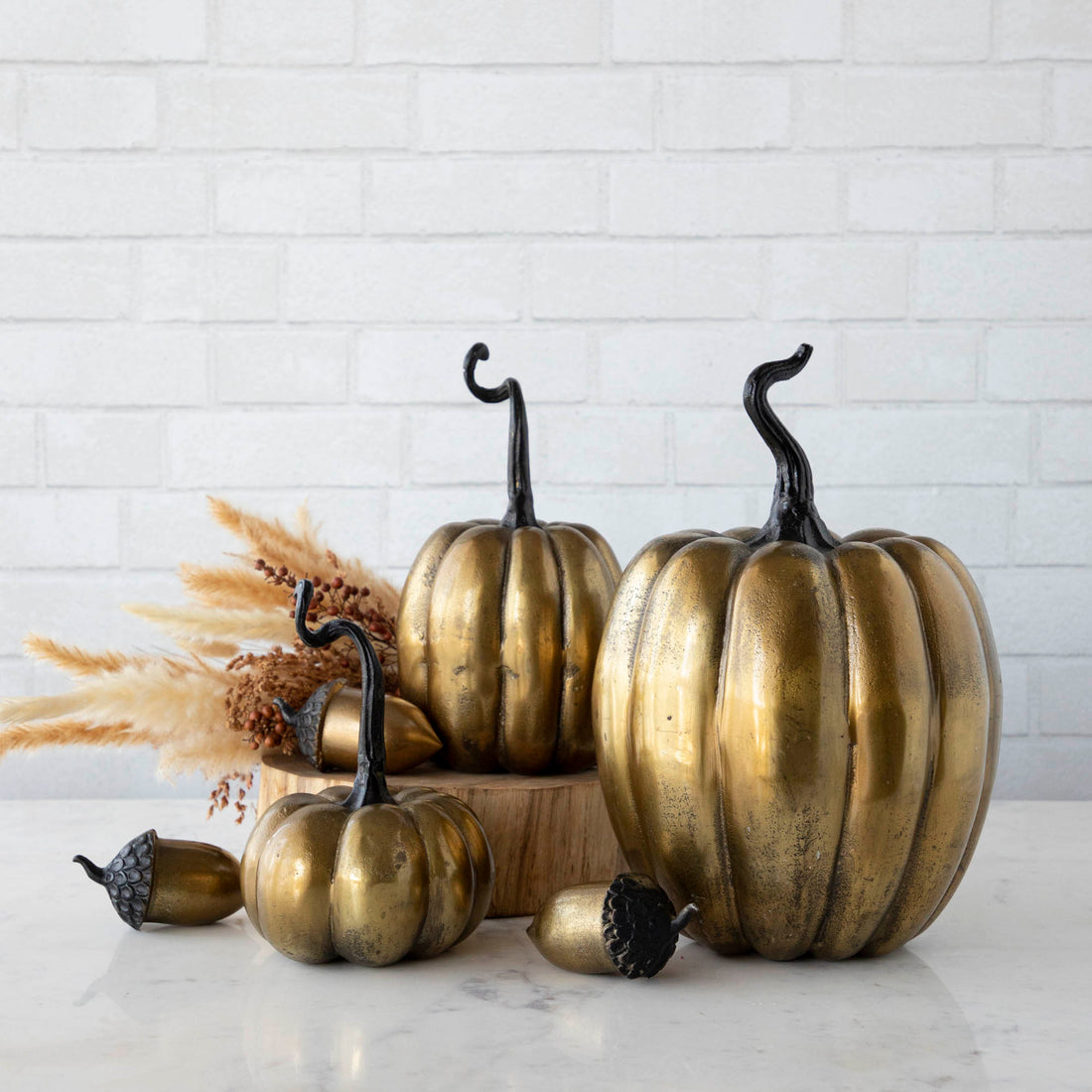 Three handmade Accent Decor brass pumpkins on a wooden table.
