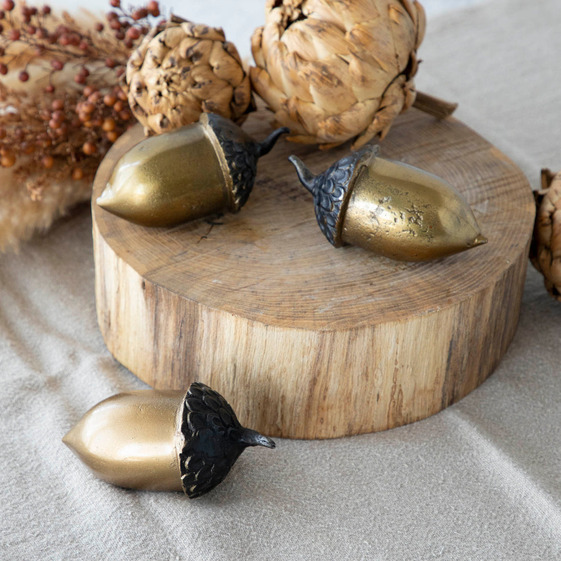 A set of three artificial brass acorns with an antique gold finish on a wooden surface.