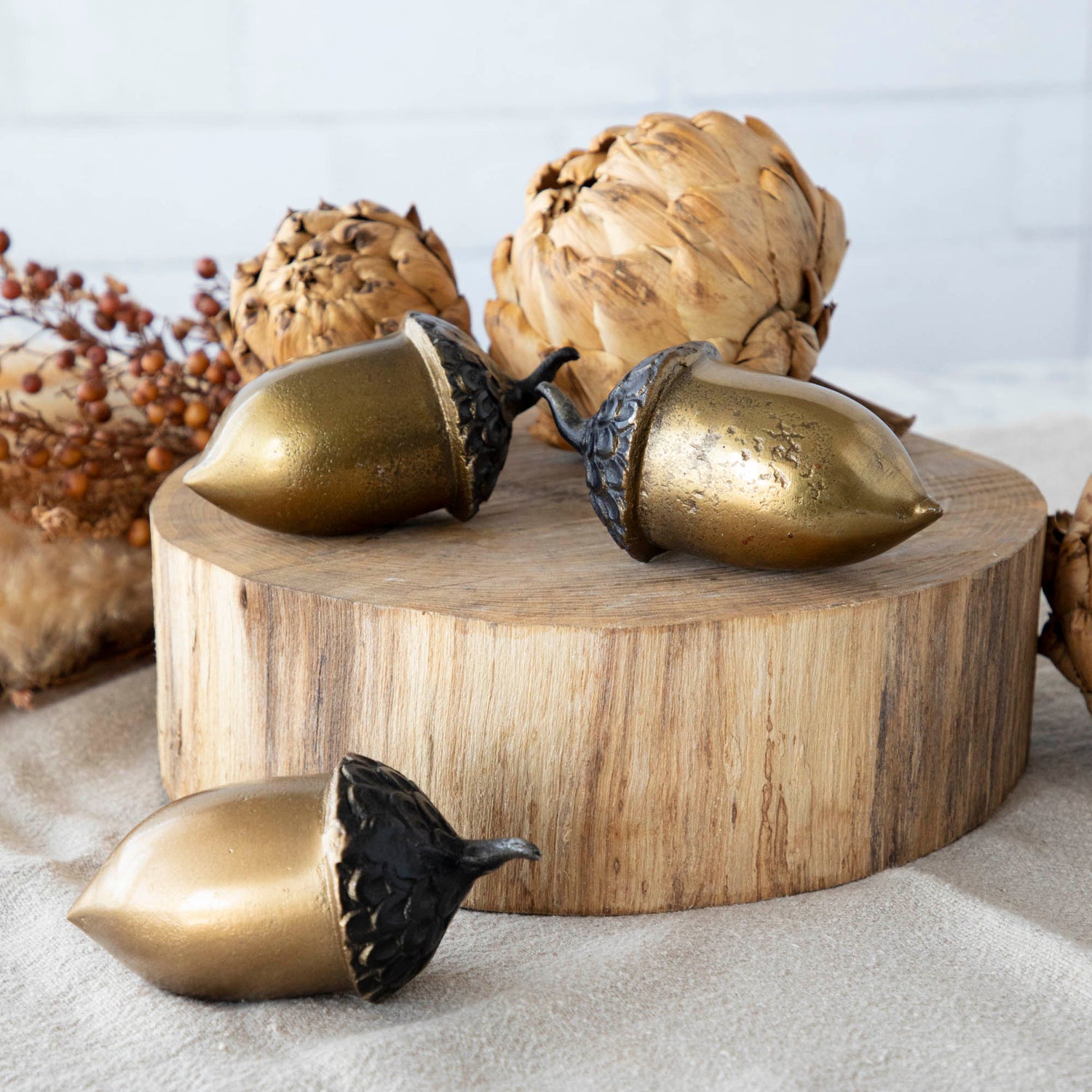 A set of three artificial brass acorns with an antique gold finish on a wooden surface.