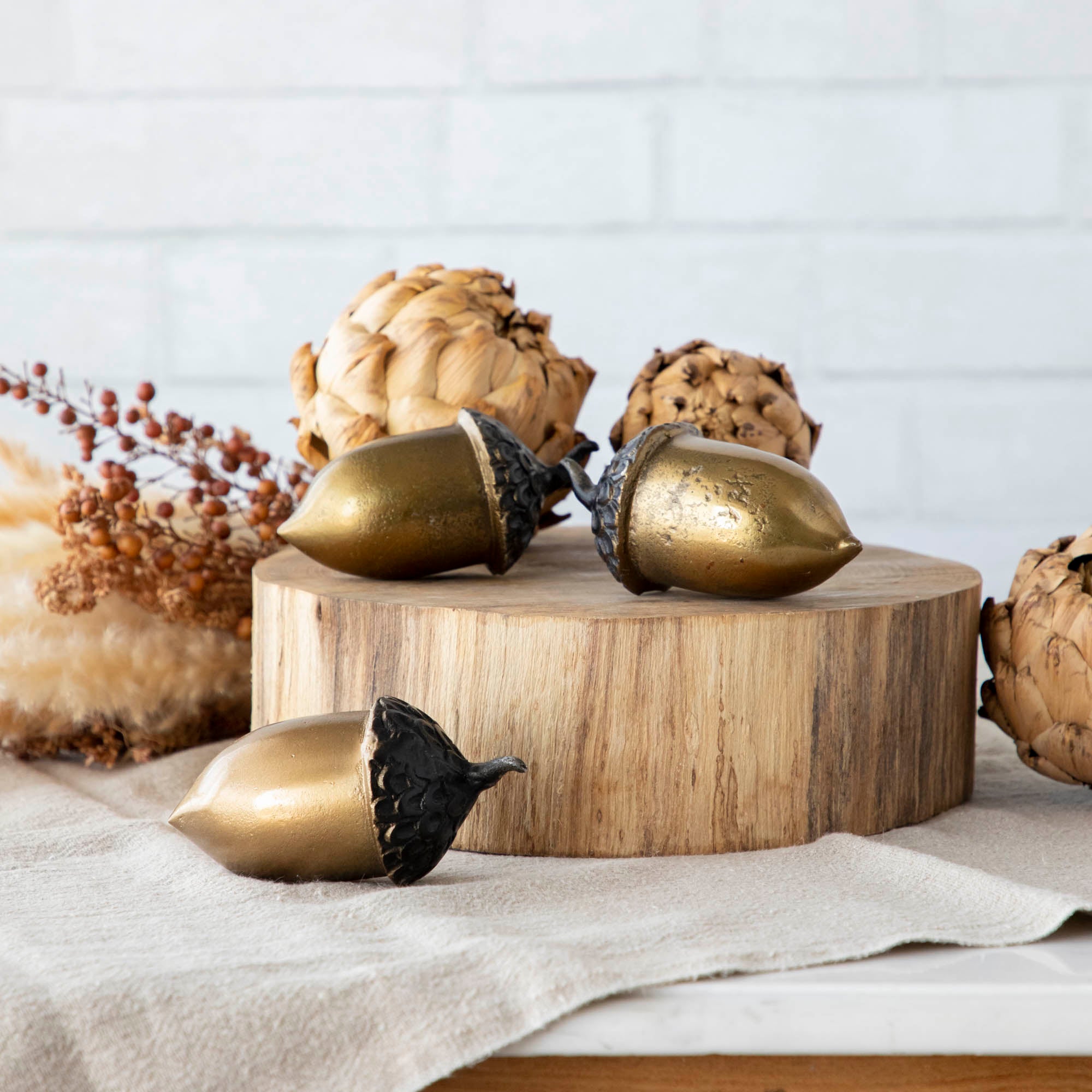 A set of three artificial brass acorns with an antique gold finish on a wooden surface.