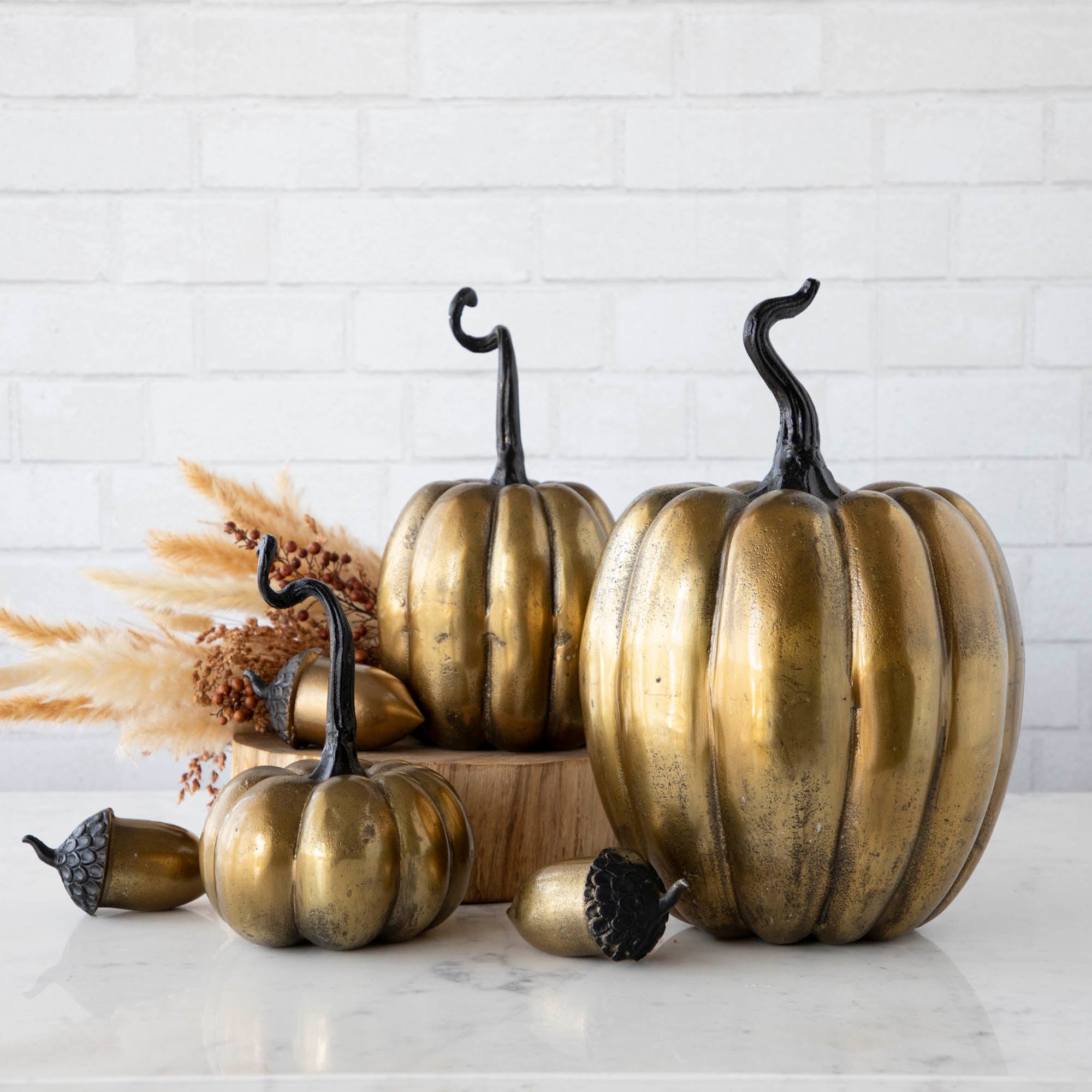 A group of artificial brass acorns and pumpkins with an antique gold finish on a wooden surface.