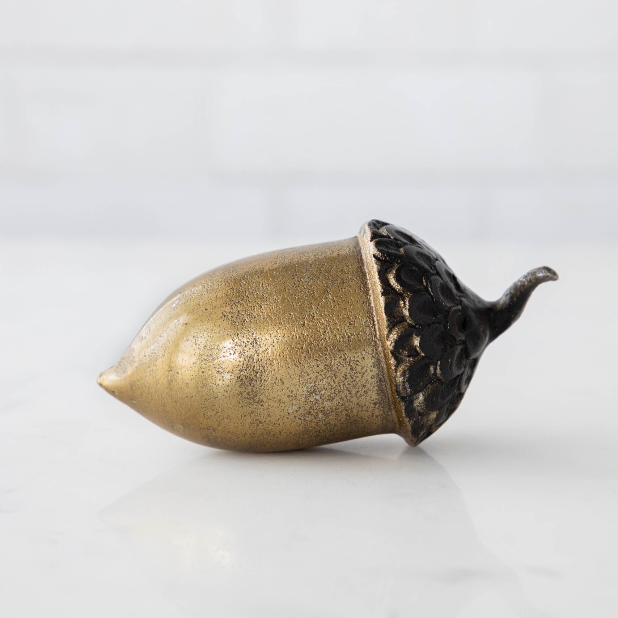 An artificial brass acorn with an antique gold finish on a white table.