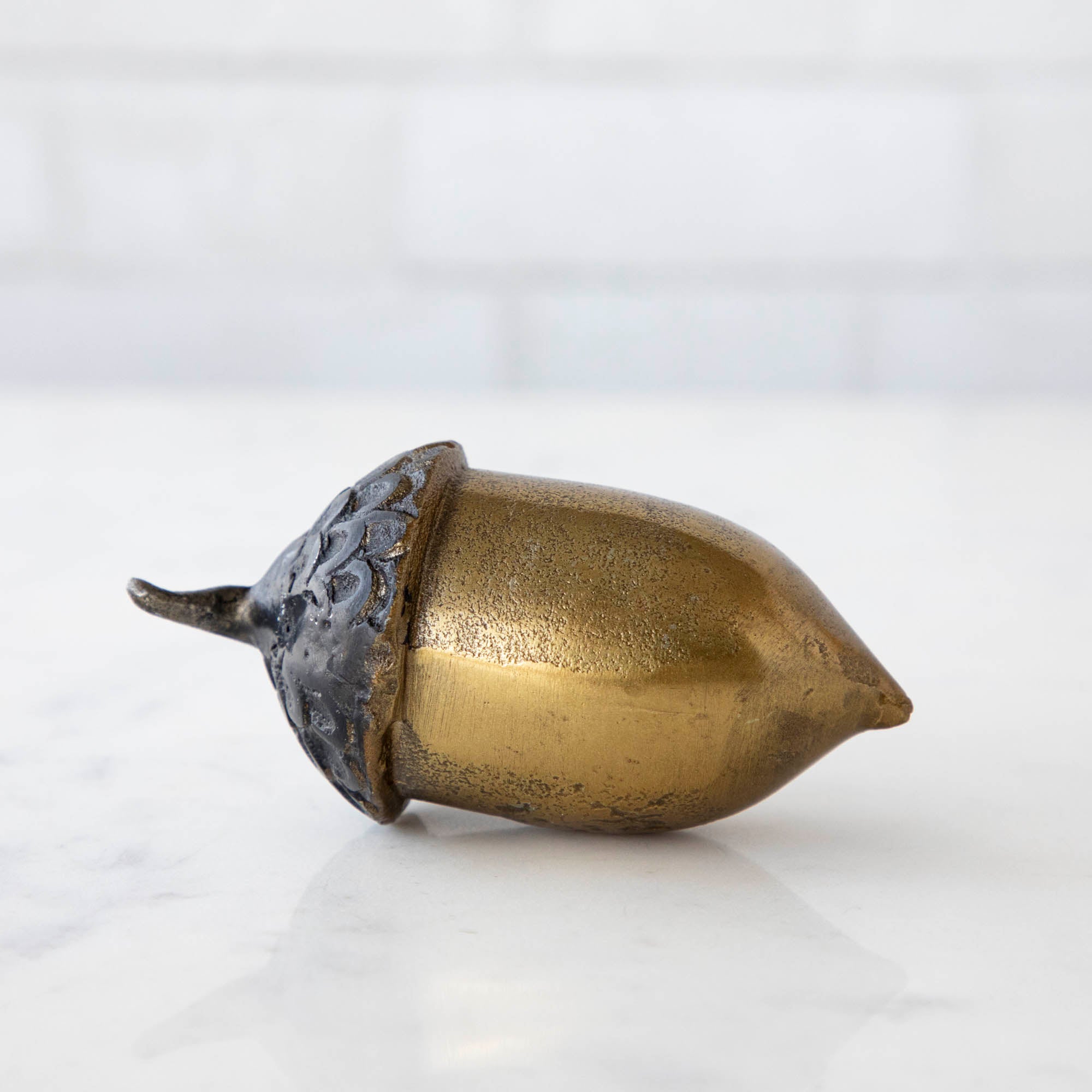 An artificial brass acorn with an antique gold finish on a white table.