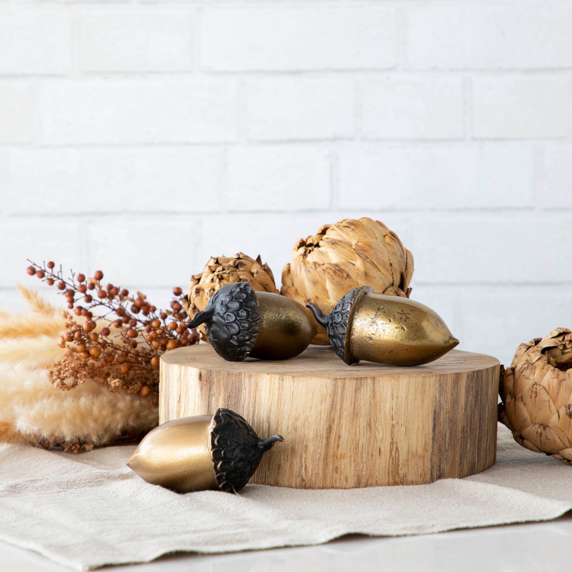 A set of three artificial brass acorns with an antique gold finish on a wooden surface.
