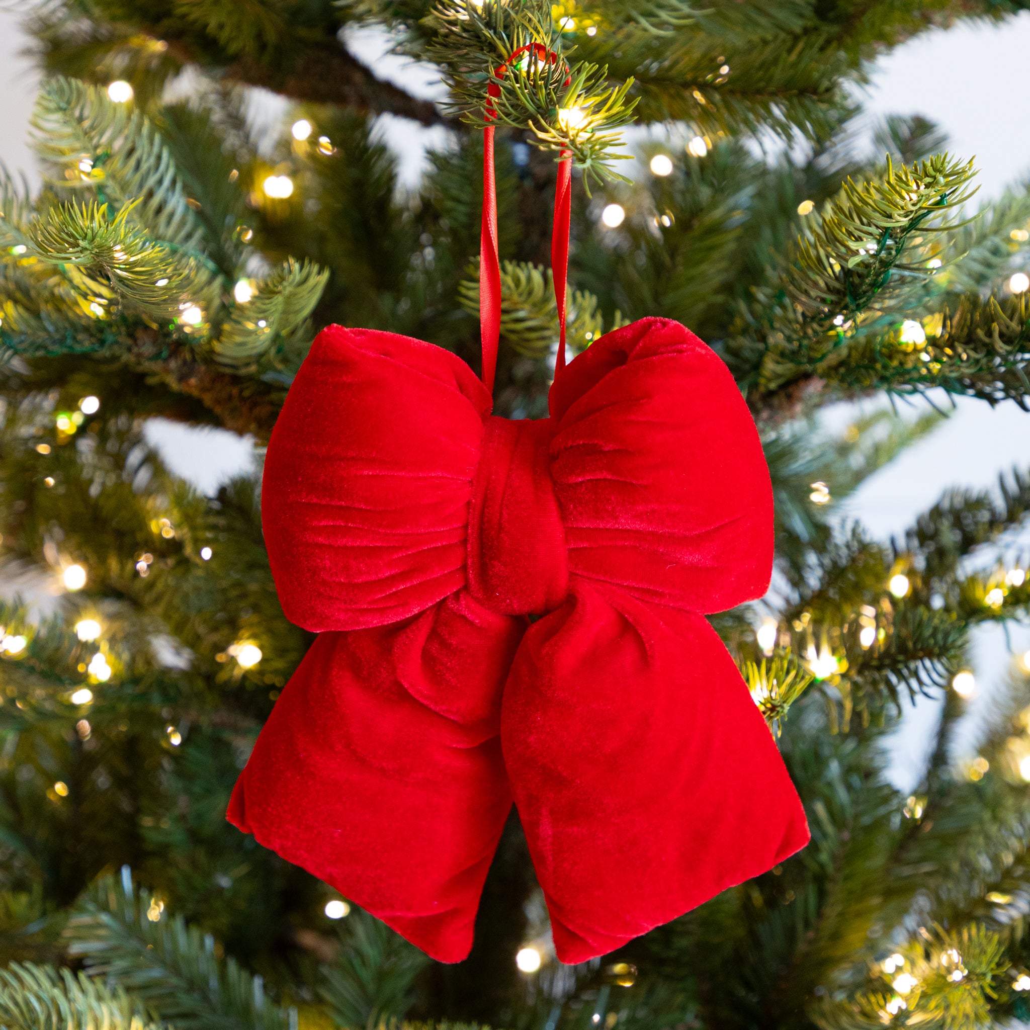 Red bow-shaped ornament on a Christmas tree with lights.
