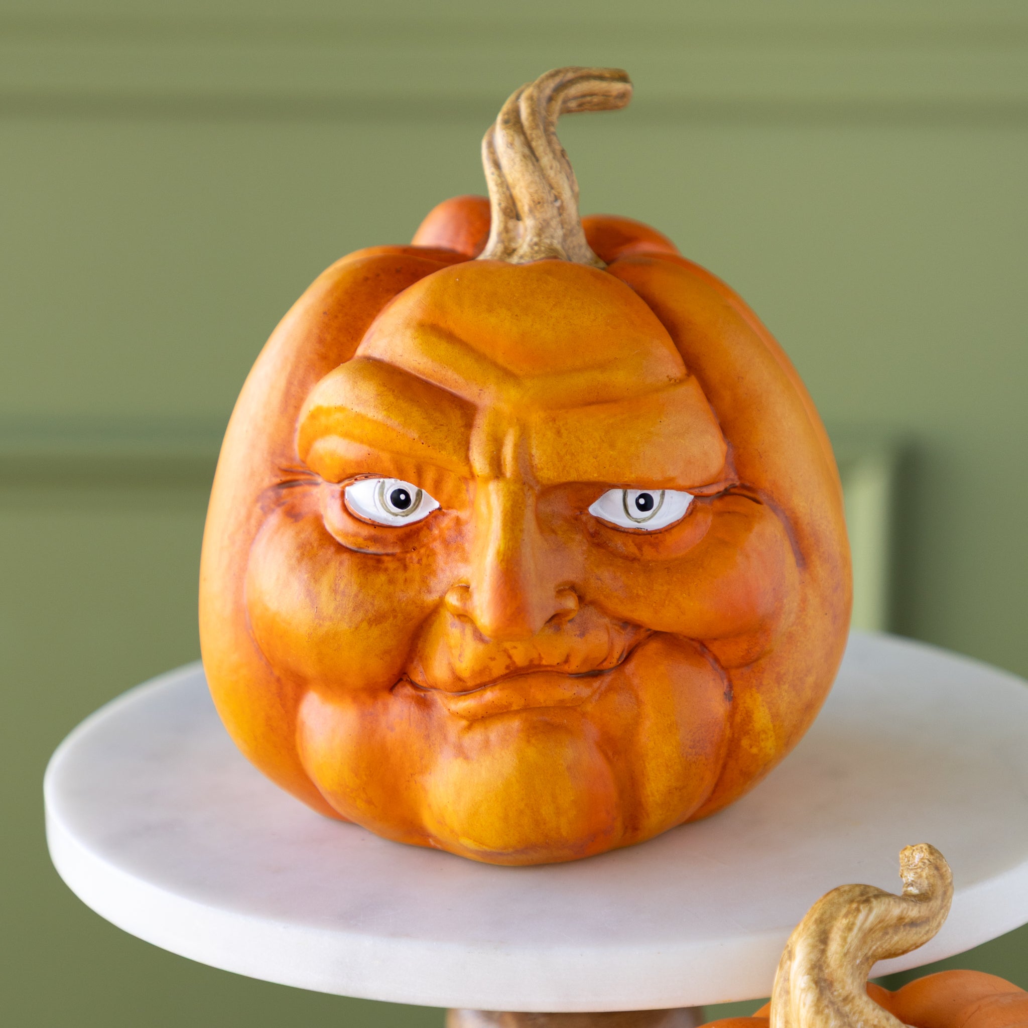 Carved pumpkin with a smirk face on a marble pedestal against a green background.