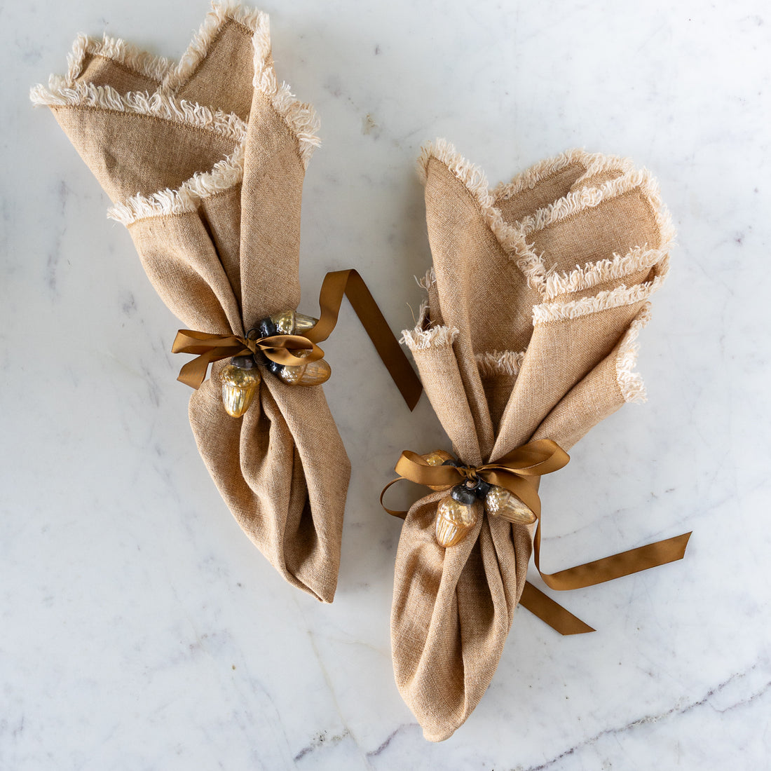 Two brown napkins tied with a brown silk ribbon and two Mercury Glass Acorn Shaped Ornaments.