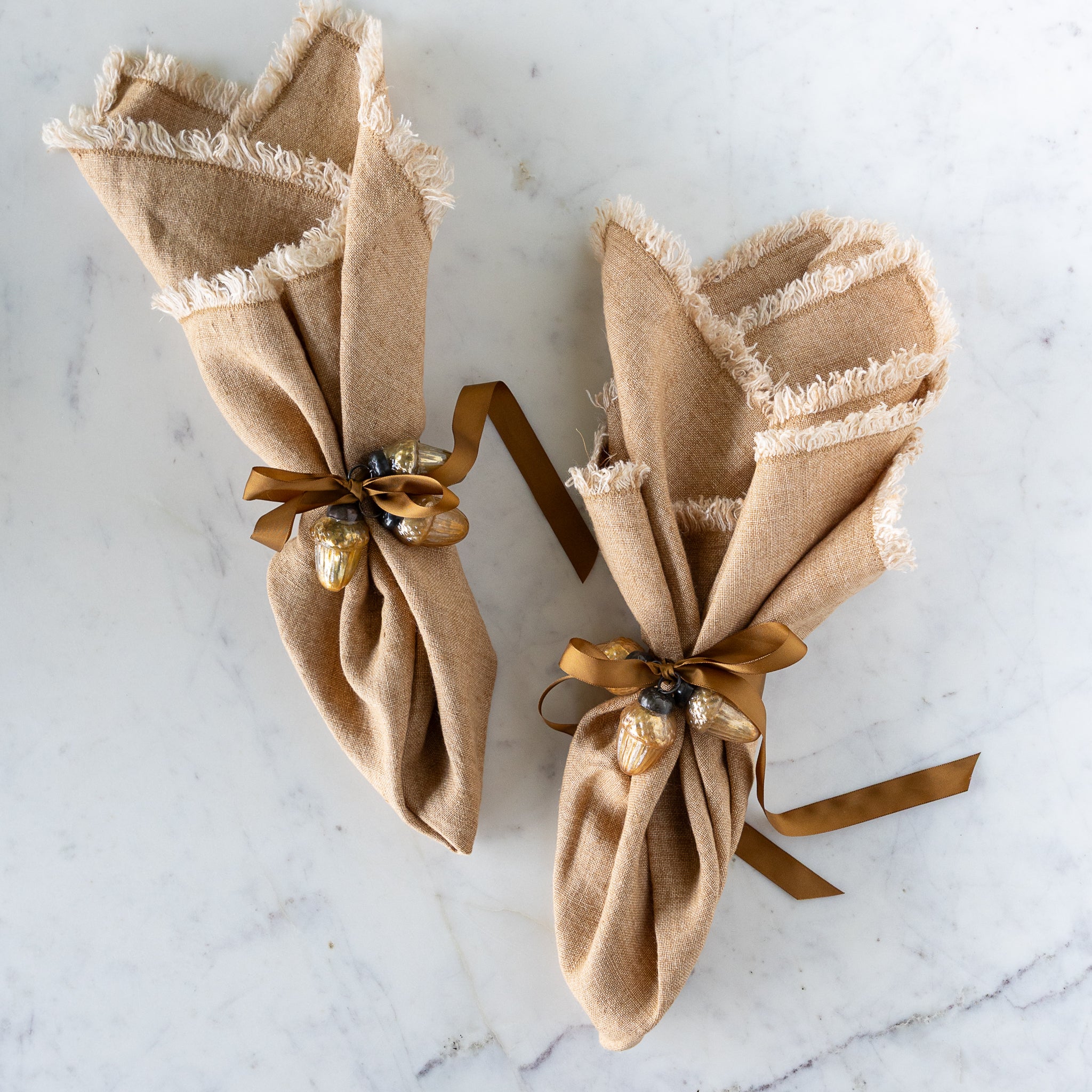 Two brown napkins tied with a brown silk ribbon and two Mercury Glass Acorn Shaped Ornaments.