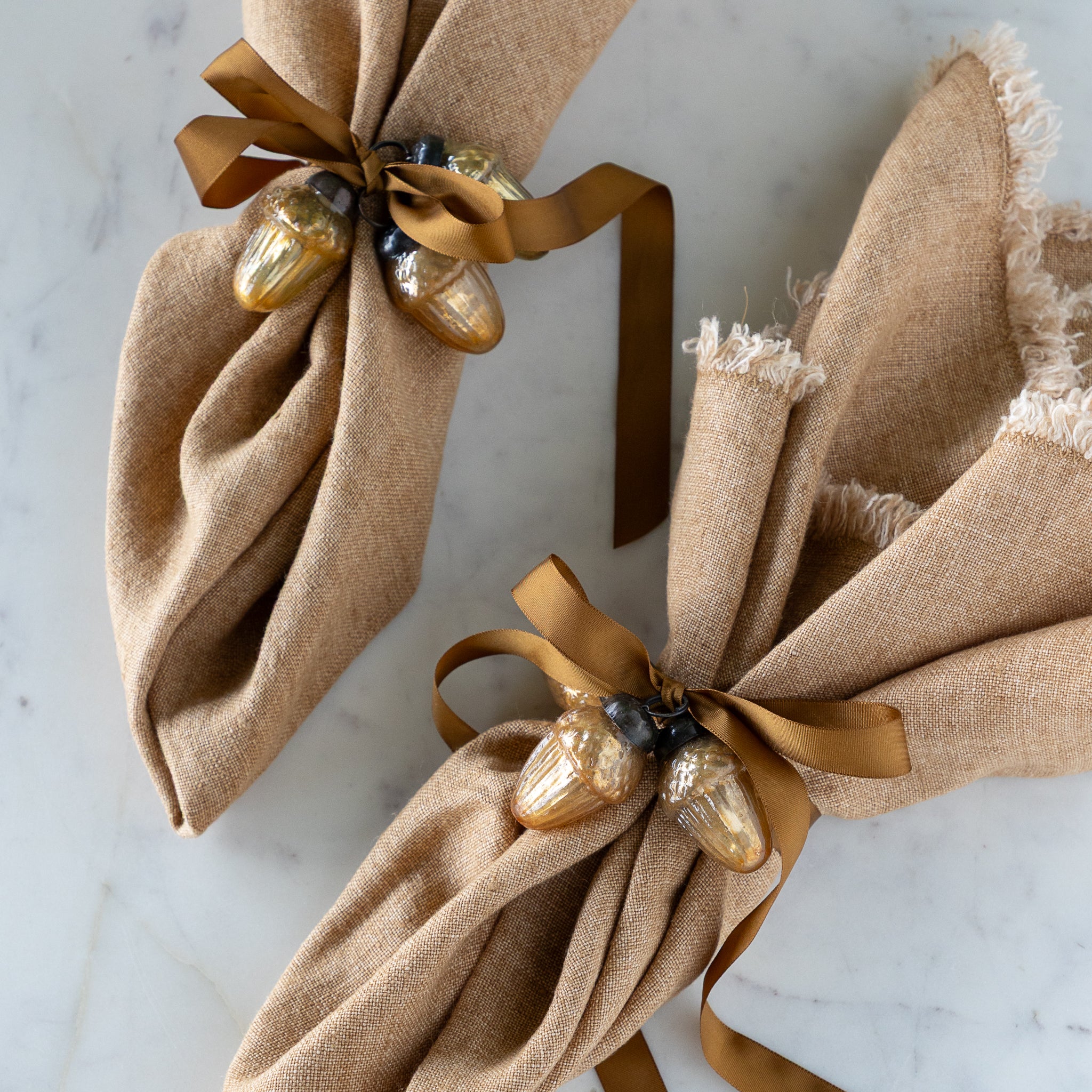 Two brown napkins tied with a brown silk ribbon and two Mercury Glass Acorn Shaped Ornaments.
