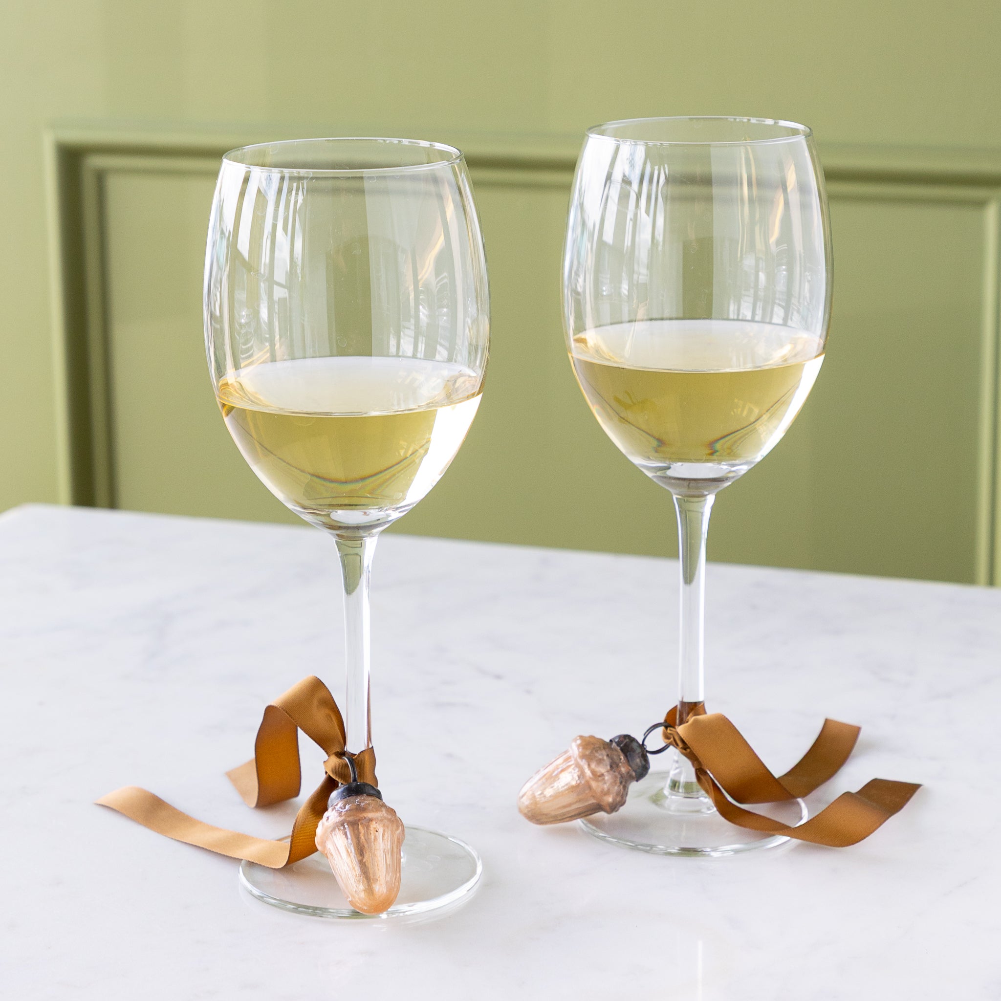 Two wine glasses with a Mercury Glass Acorn Shaped Ornaments tied at the bottom with a silk brown ribbon.