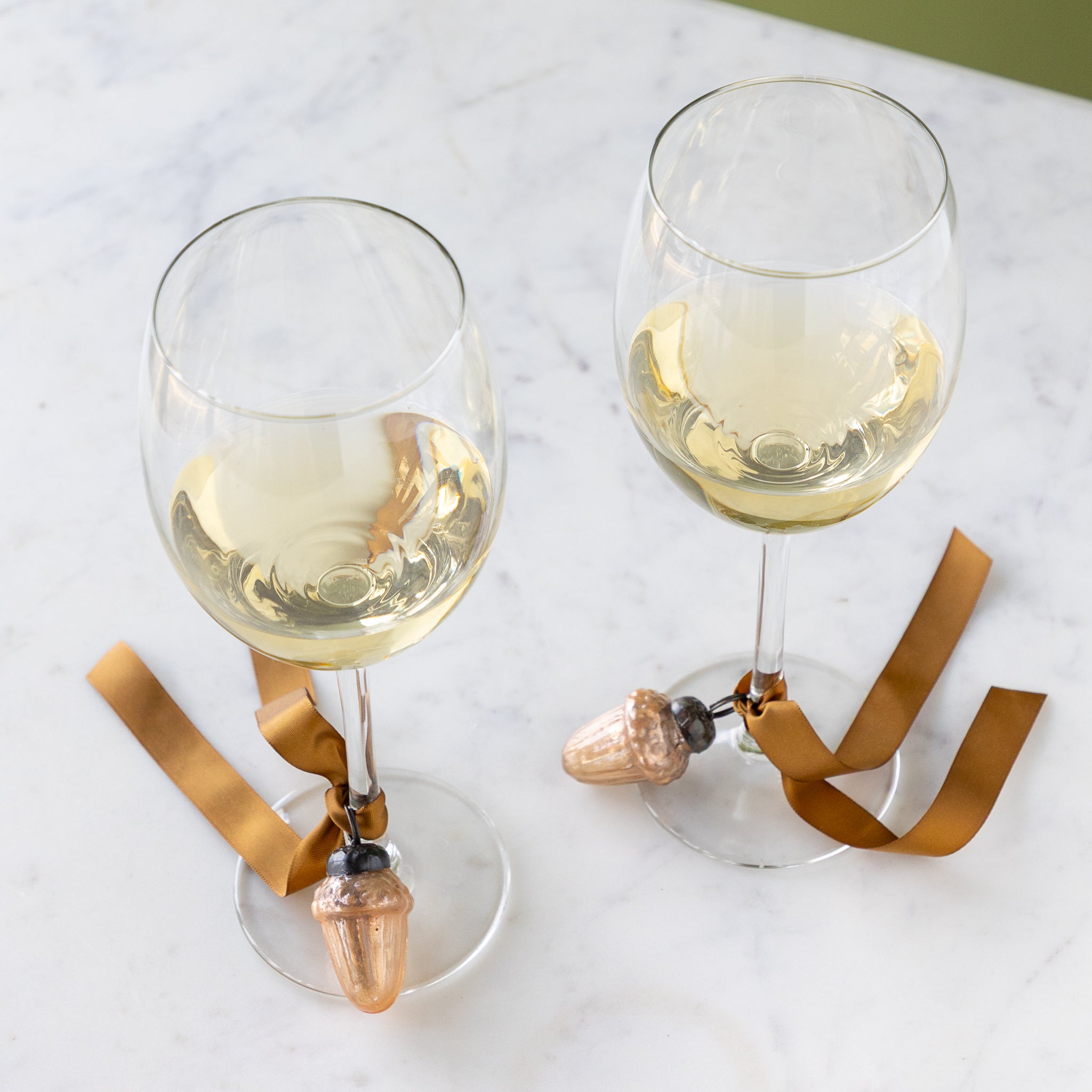 Two wine glasses with a Mercury Glass Acorn Shaped Ornaments tied at the bottom with a silk brown ribbon.