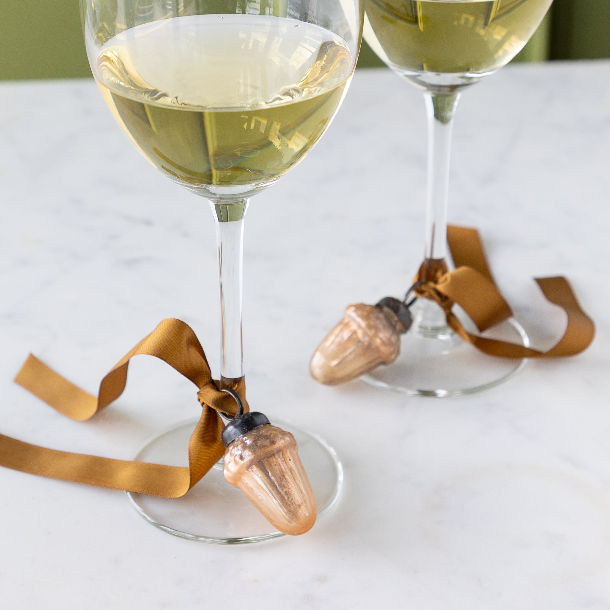 Two wine glasses with a Mercury Glass Acorn Shaped Ornaments tied at the bottom with a silk brown ribbon.