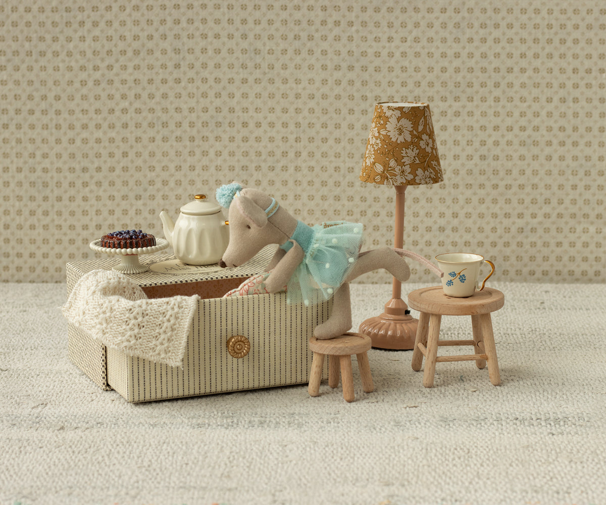 Miniature tea set with mouse and lamp in a room with patterned wallpaper.
