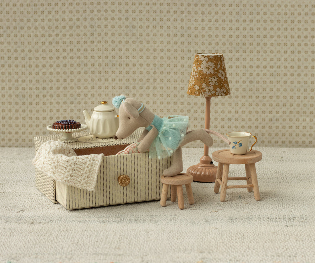 Miniature tea set with mouse and lamp in a room with patterned wallpaper.