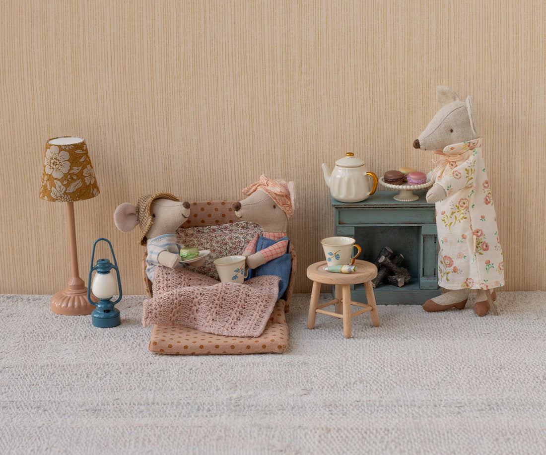 Miniature scene with toy mice and furniture against a striped wall.