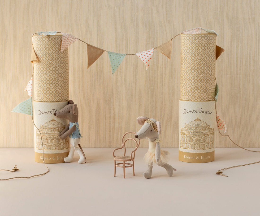Two stuffed animal toys with decorative boxes and a string of flags on a neutral background. 