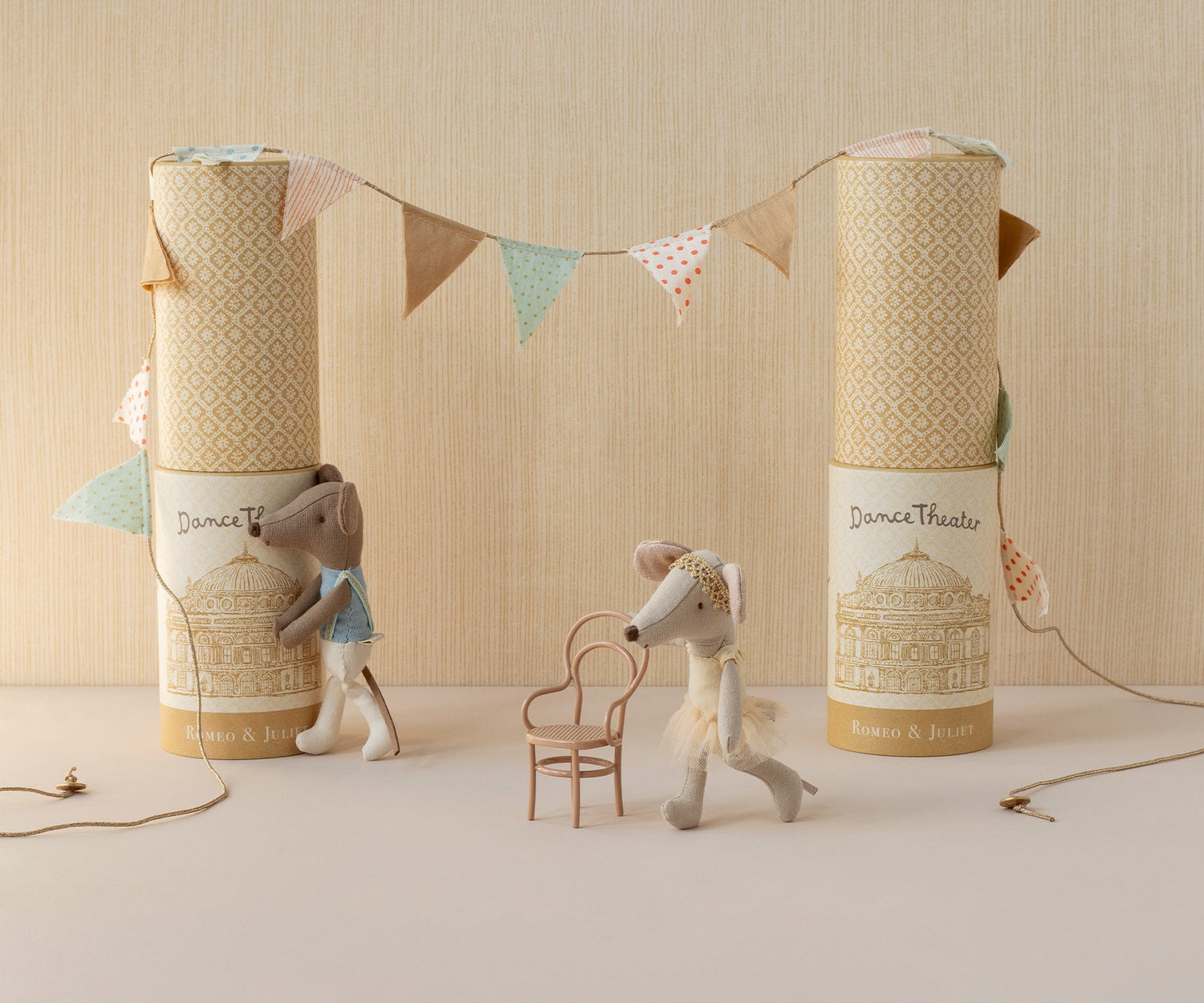 Two stuffed animal toys with decorative boxes and a string of flags on a neutral background. 