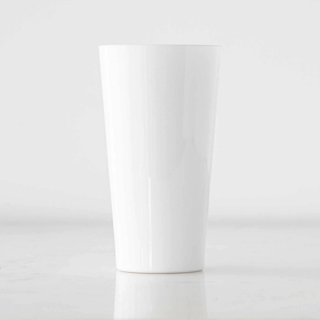 A white, solid-colored pint glass made from durable material, displayed against a neutral background.