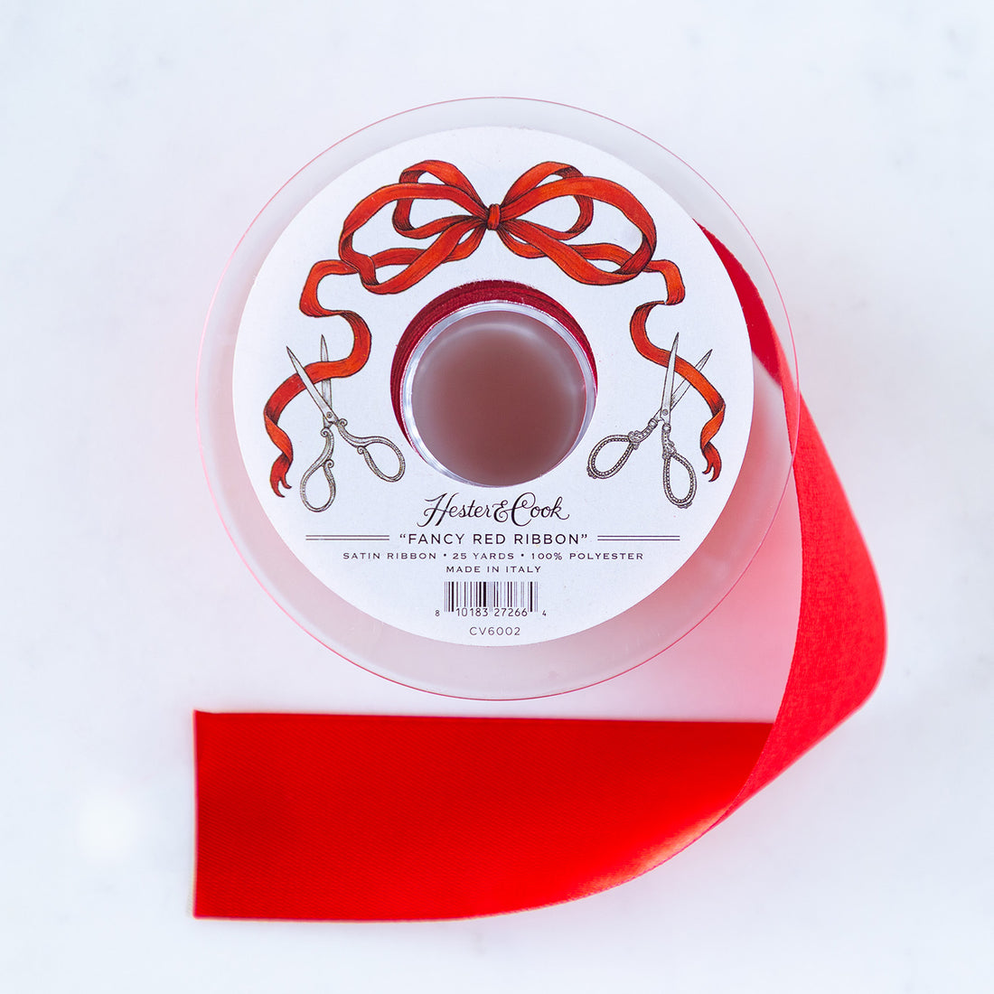 A spool of red satin ribbon with a label featuring illustrated scissors and red bow branded "Hester & Cook Fancy Red Ribbon.