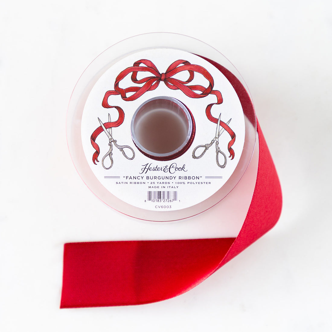 A spool of burgundy satin ribbon with a label featuring illustrated scissors and a red bow, branded "Hester & Cook Fancy Olive Ribbon.