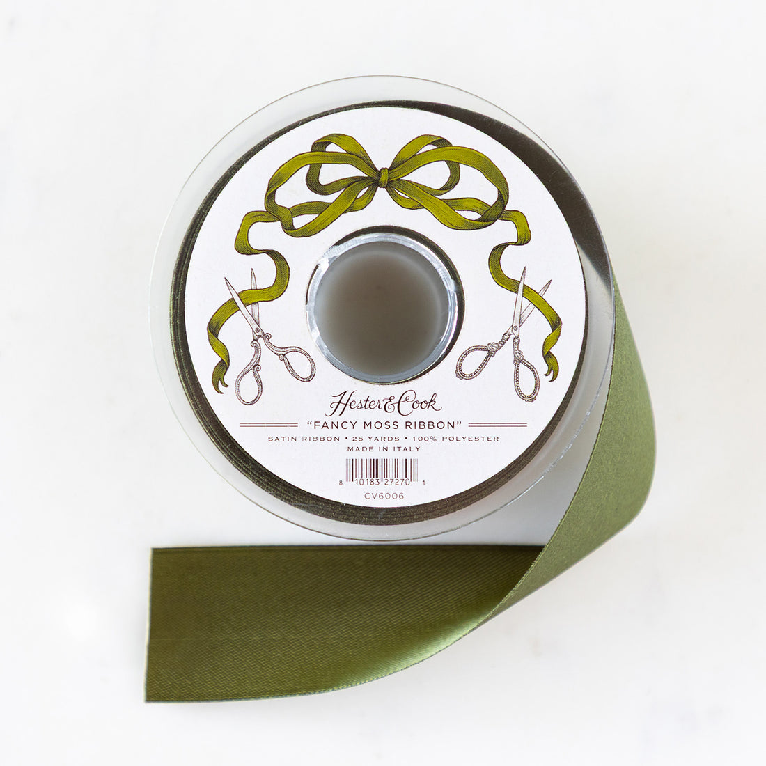A spool of moss-green satin ribbon with a label featuring illustrated scissors and moss bow, branded "Hester & Cook Fancy Moss Ribbon.