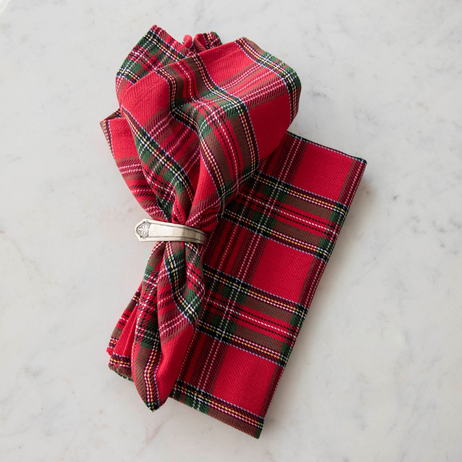 Two red plaid cotton napkins, one folded and one in a napkin ring, displayed on a white surface.