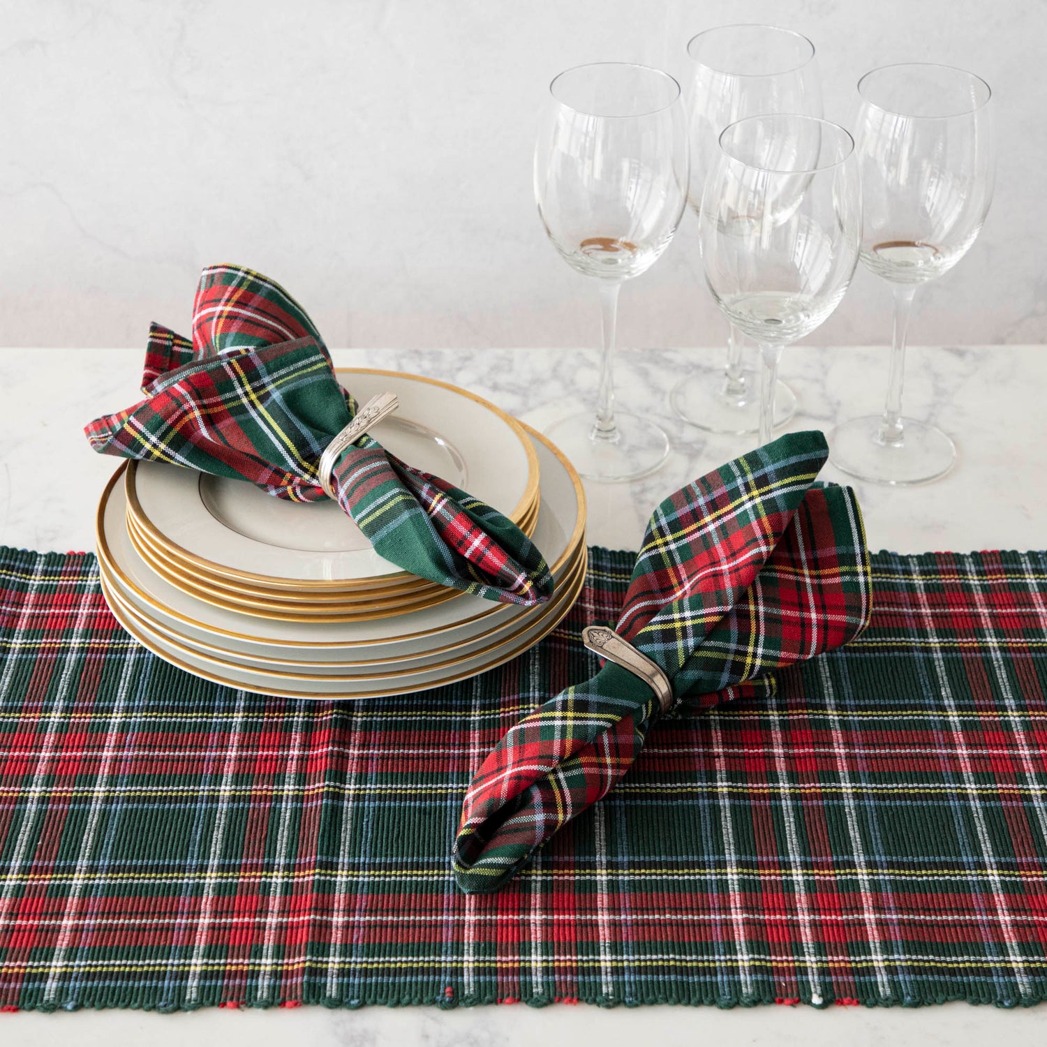 Two green and red plaid cotton napkins in napkin rings, on a table set with a matching plaid runner. 