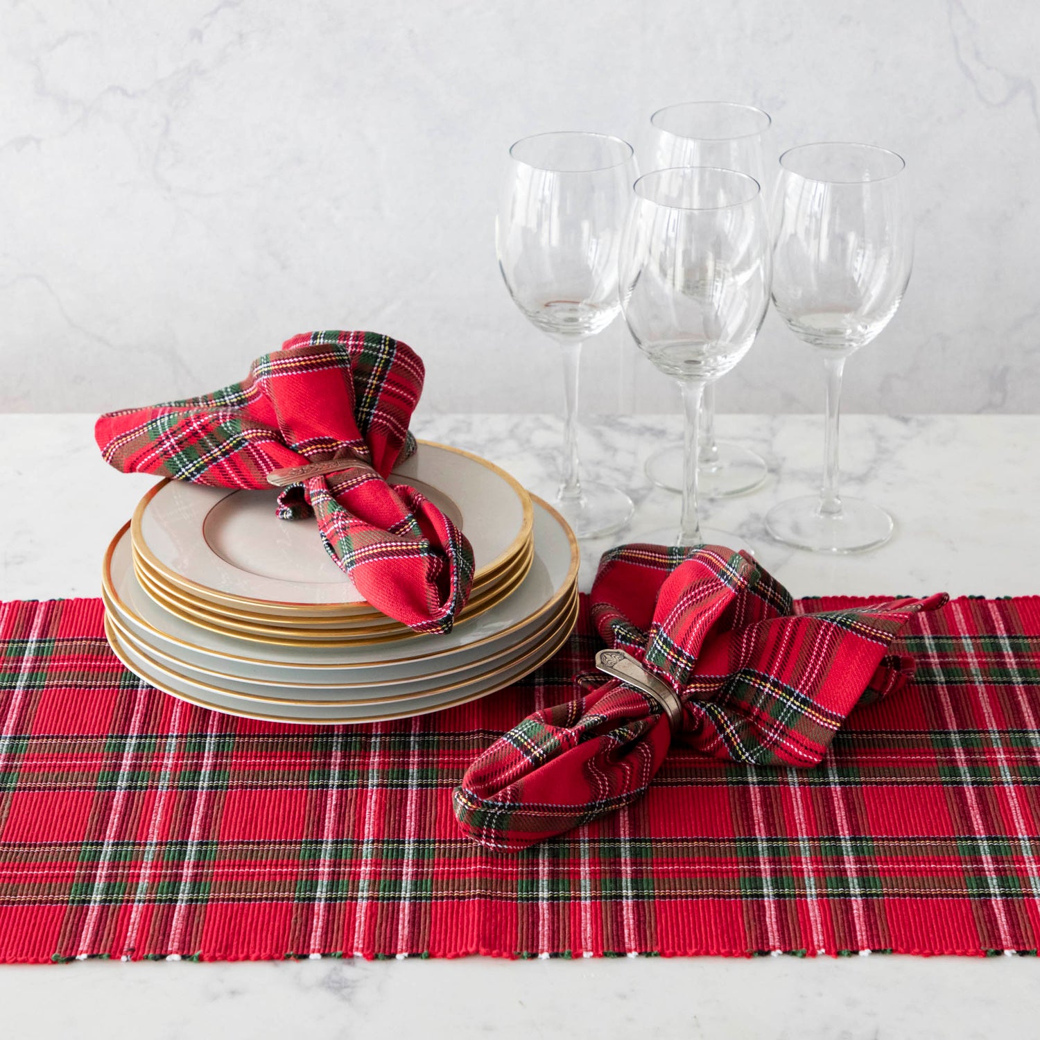 Two red plaid cotton napkins in napkin rings, on a table set with a matching plaid runner. 