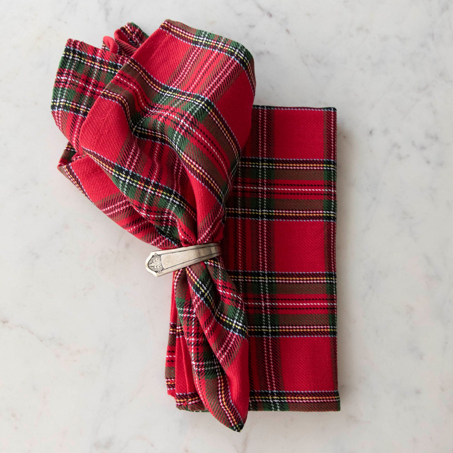 Two red plaid cotton napkins, one folded and one in a napkin ring, displayed on a white surface.