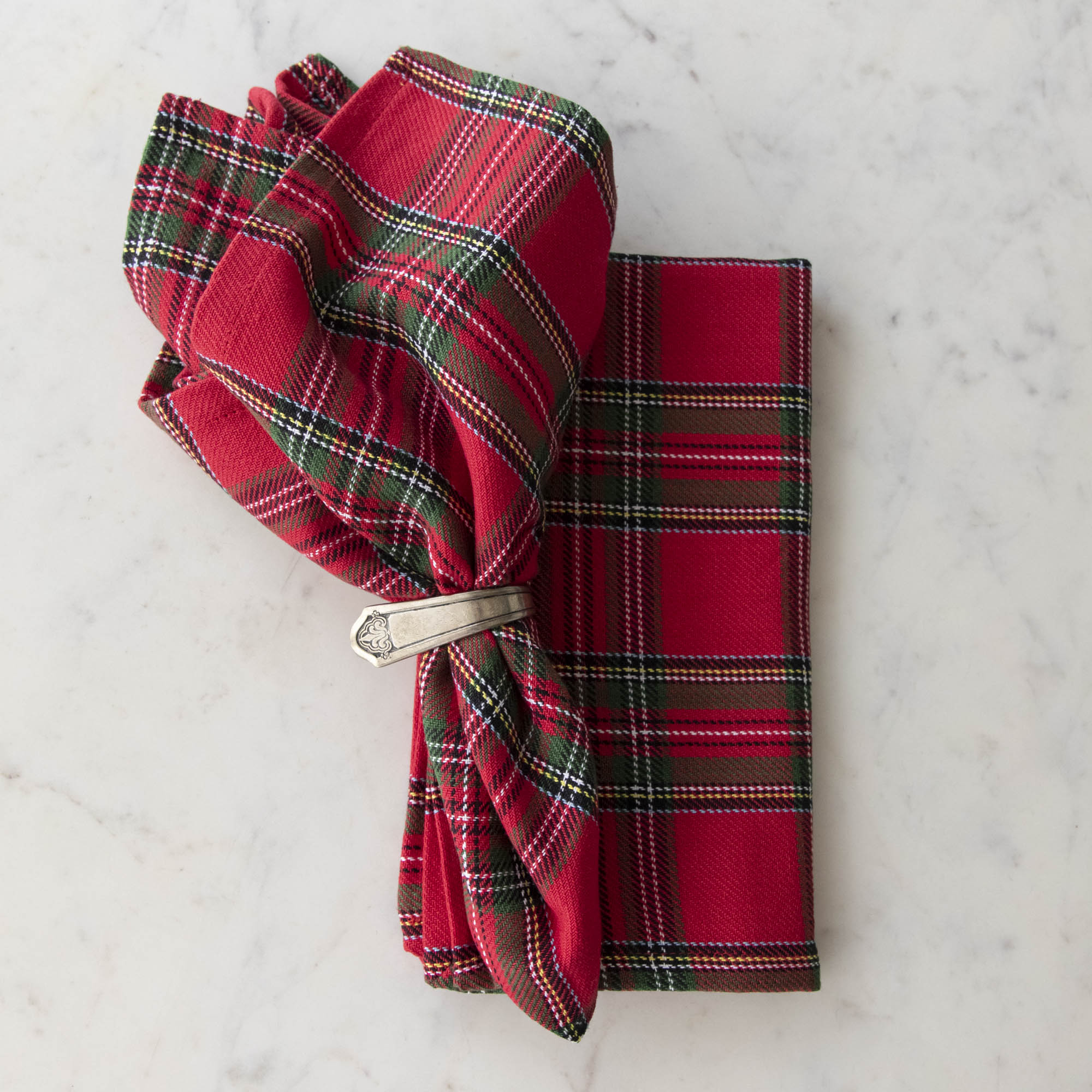 Two red plaid cotton napkins, one folded and one in a napkin ring, displayed on a white surface.