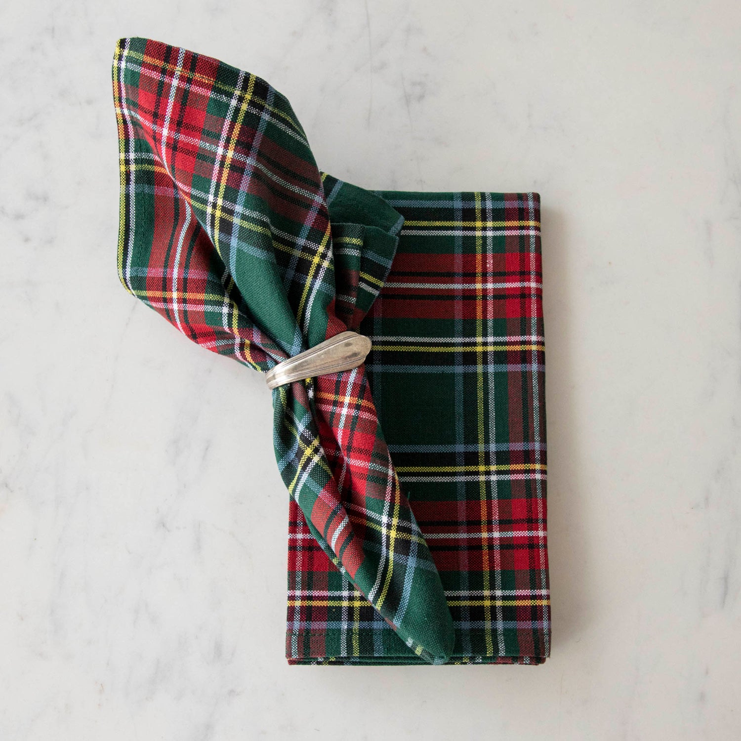 Two green and red plaid cotton napkins, one folded and one in a napkin ring, displayed on a white surface.