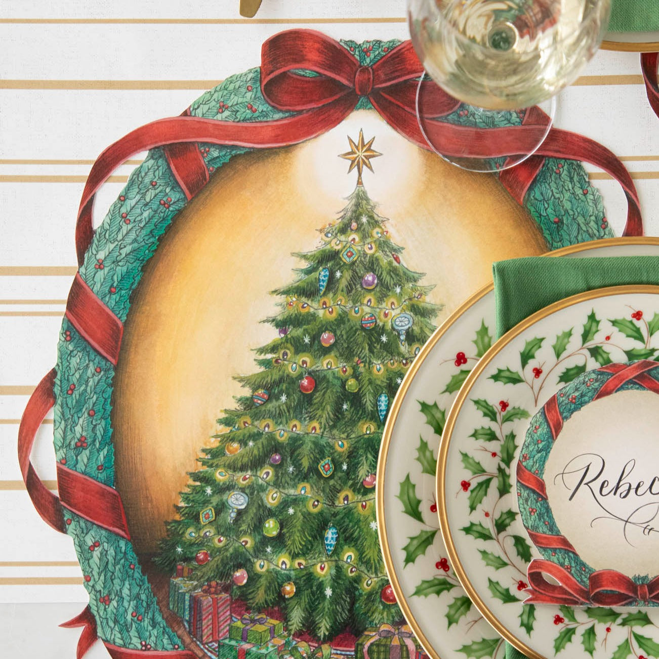 Close-up view of a Die-cut Christmas Tree Wreath Placemat with holly themed dinner plates on top and a wine glass.