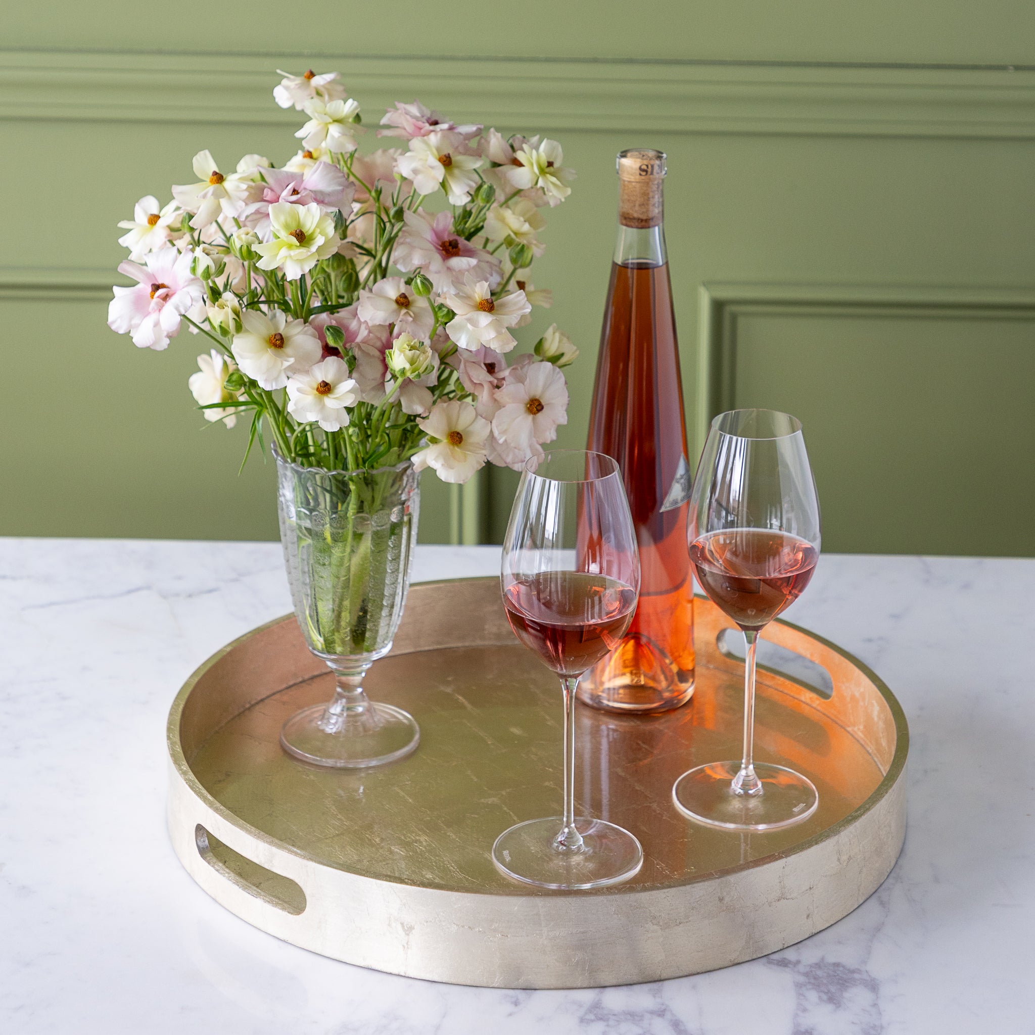 Champagne Silver Round Foiled Tray with two wine glasses, a bottle of wine and a vase of flowers in it.