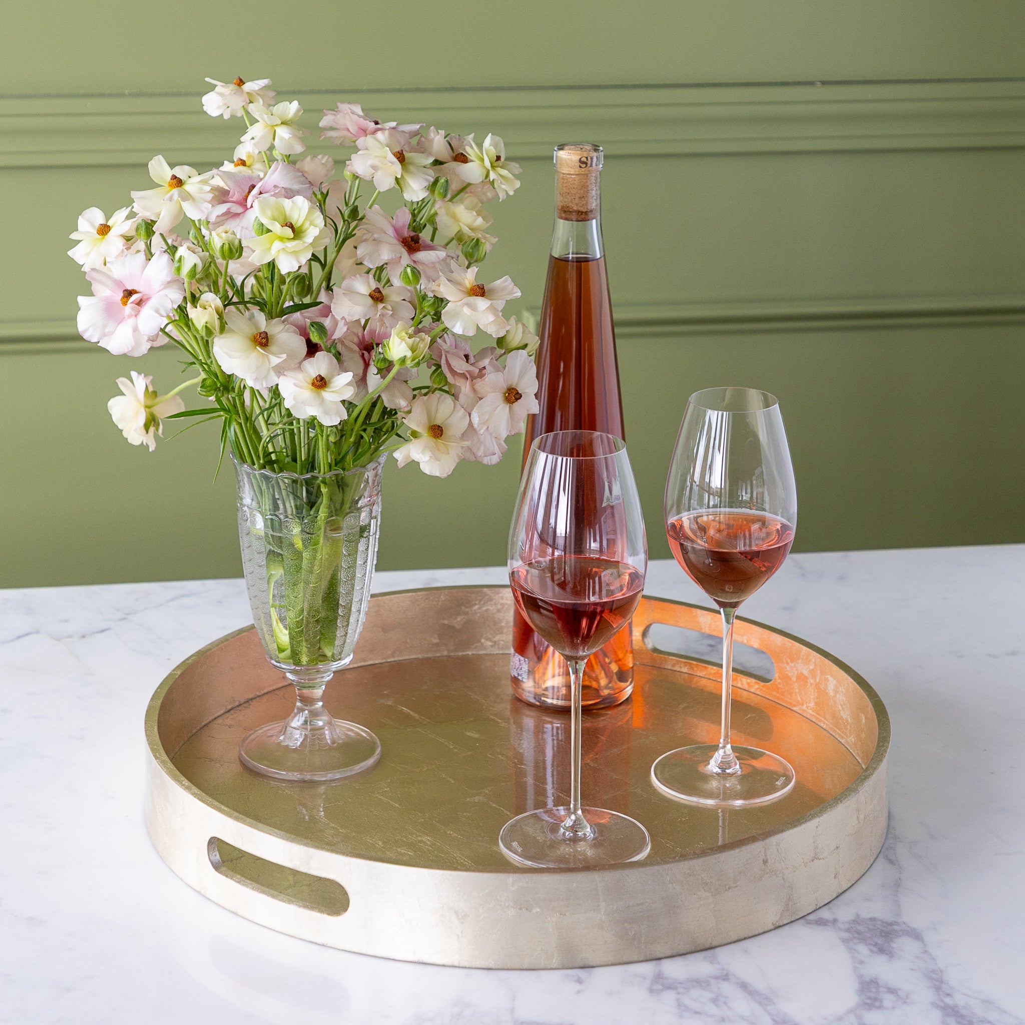 Champagne Silver Round Foiled Tray with two wine glasses, a bottle of wine and a vase of flowers in it.